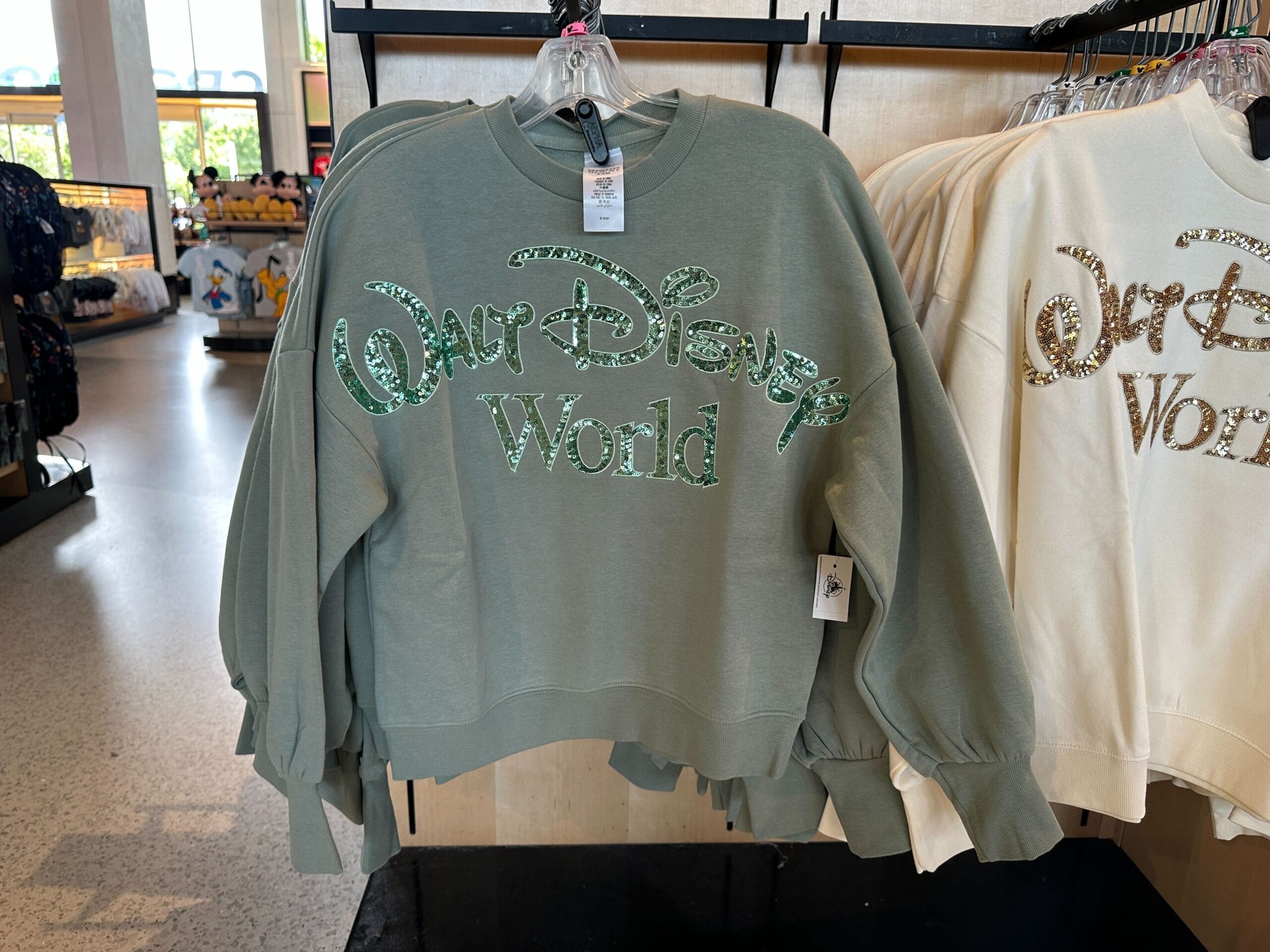 Green Walt Disney World sweatshirt with shiny lettering, a must-have piece of WDW merch, hangs in a retail store.