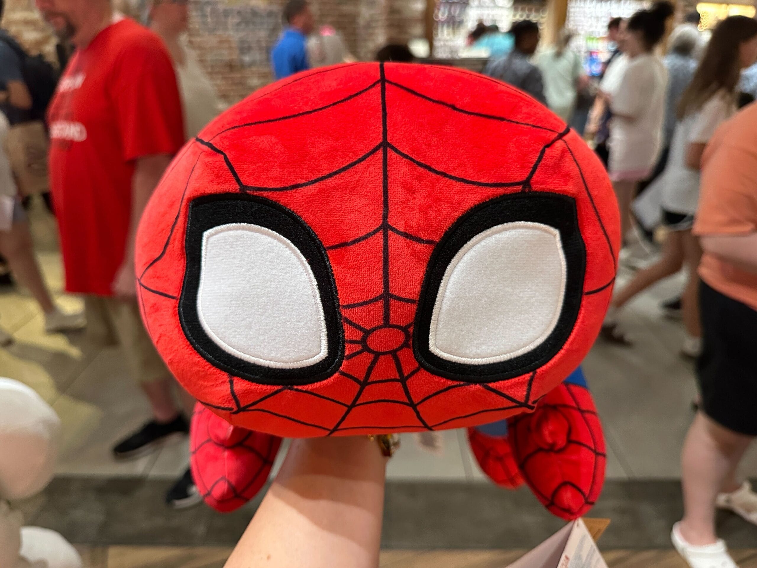 A person holds a plush toy of Spider-Man in a crowded store.