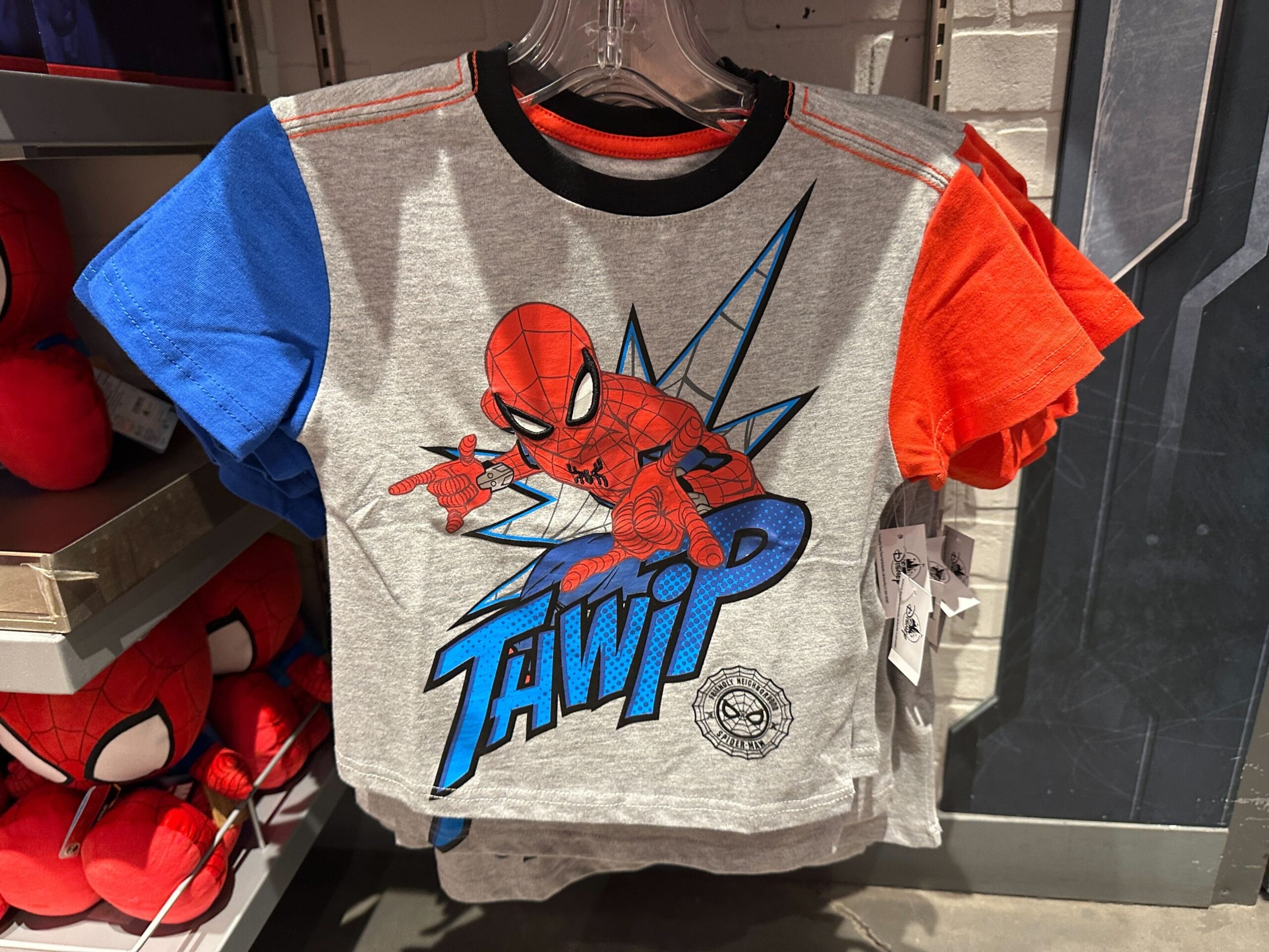 Children’s T-shirt with Spider-Man graphic, part of Marvel Merchandise, featuring red and blue sleeves, hanging in a store.