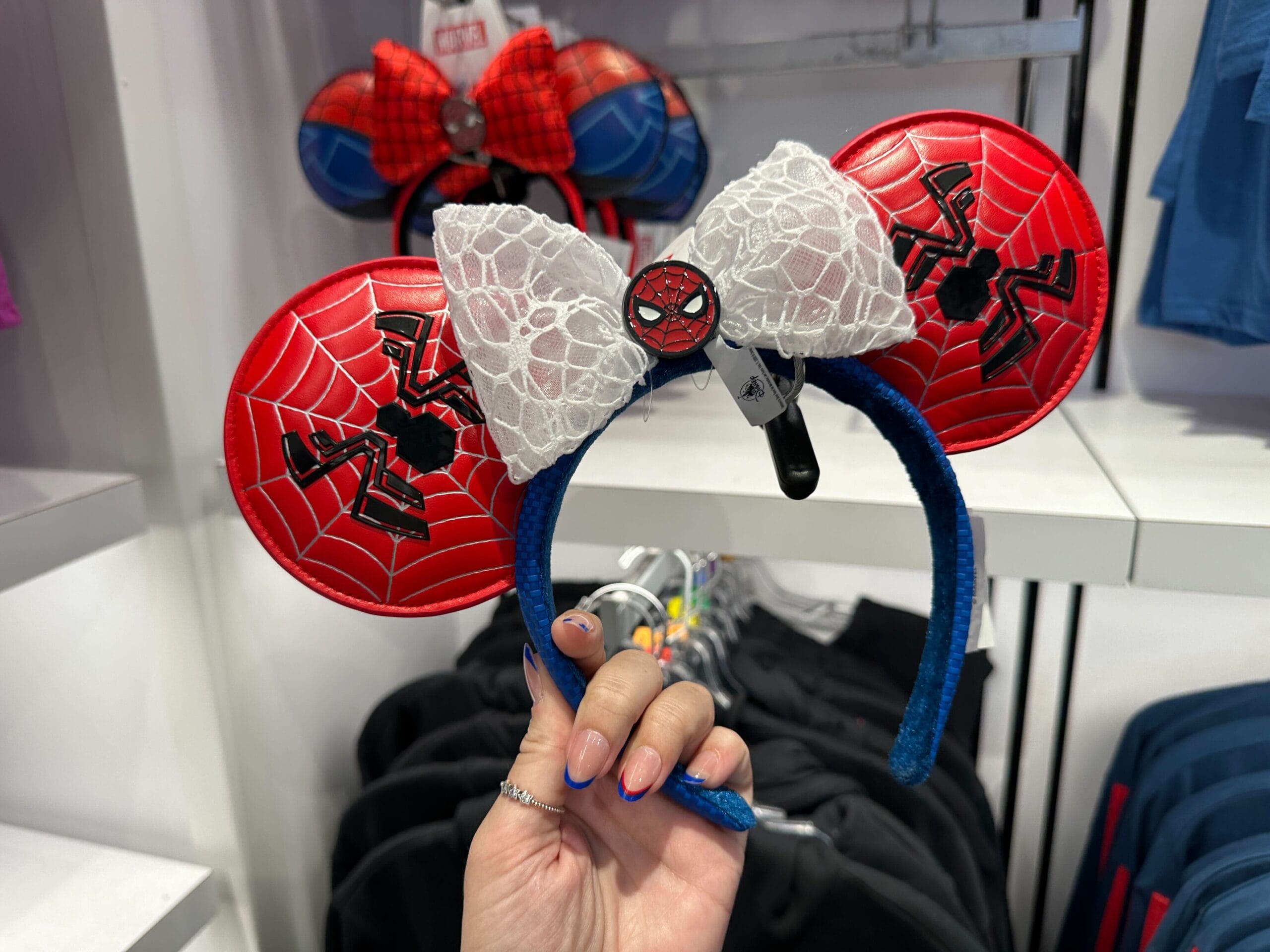 A hand holding Marvel merchandise: Spider-Man themed Mickey ears headband with a white lace bow and red webbed ears.
