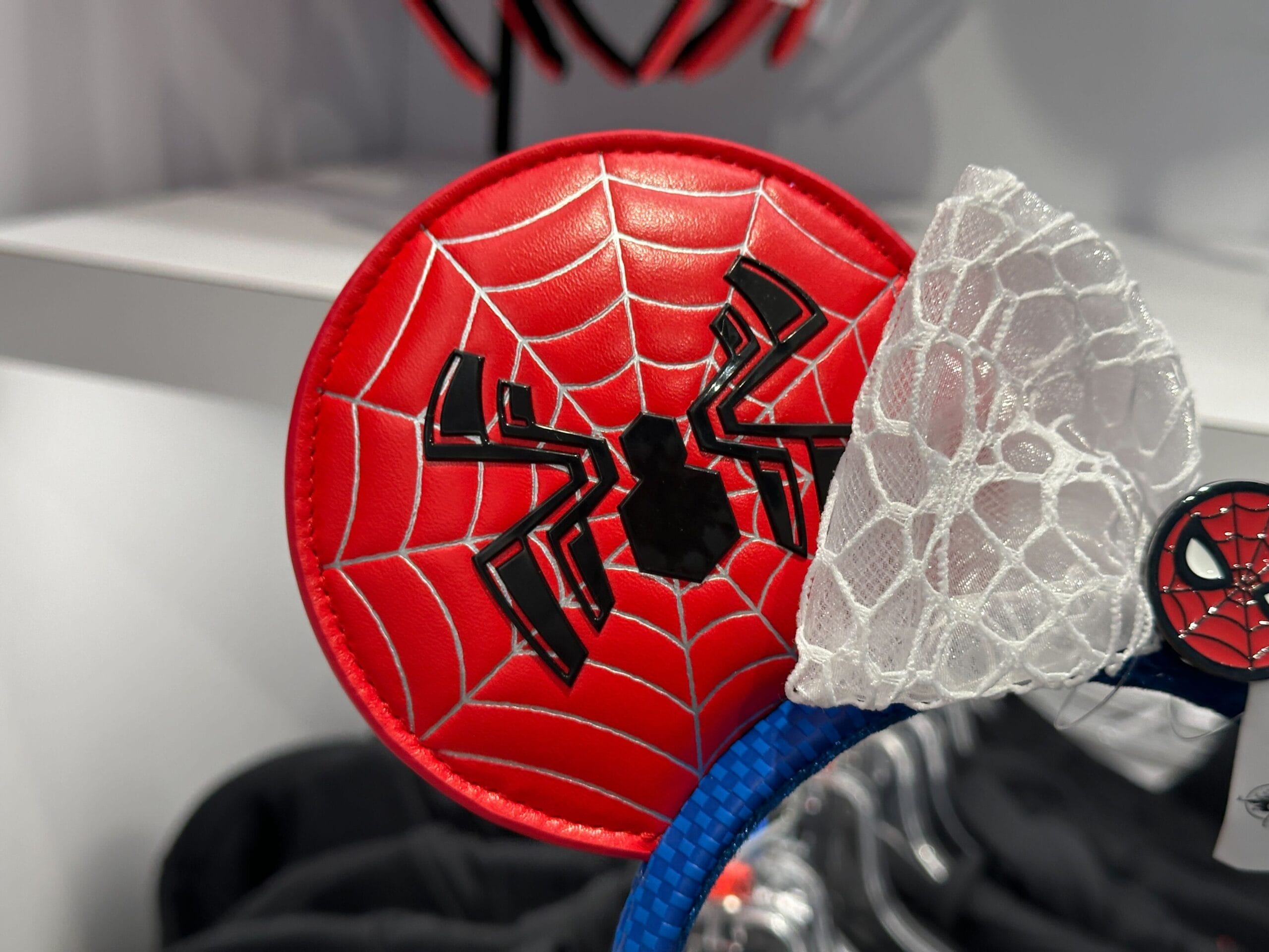 Red and black Spider-Man ear headband with web design, a white lace bow, and Marvel merchandise on display in a store.
