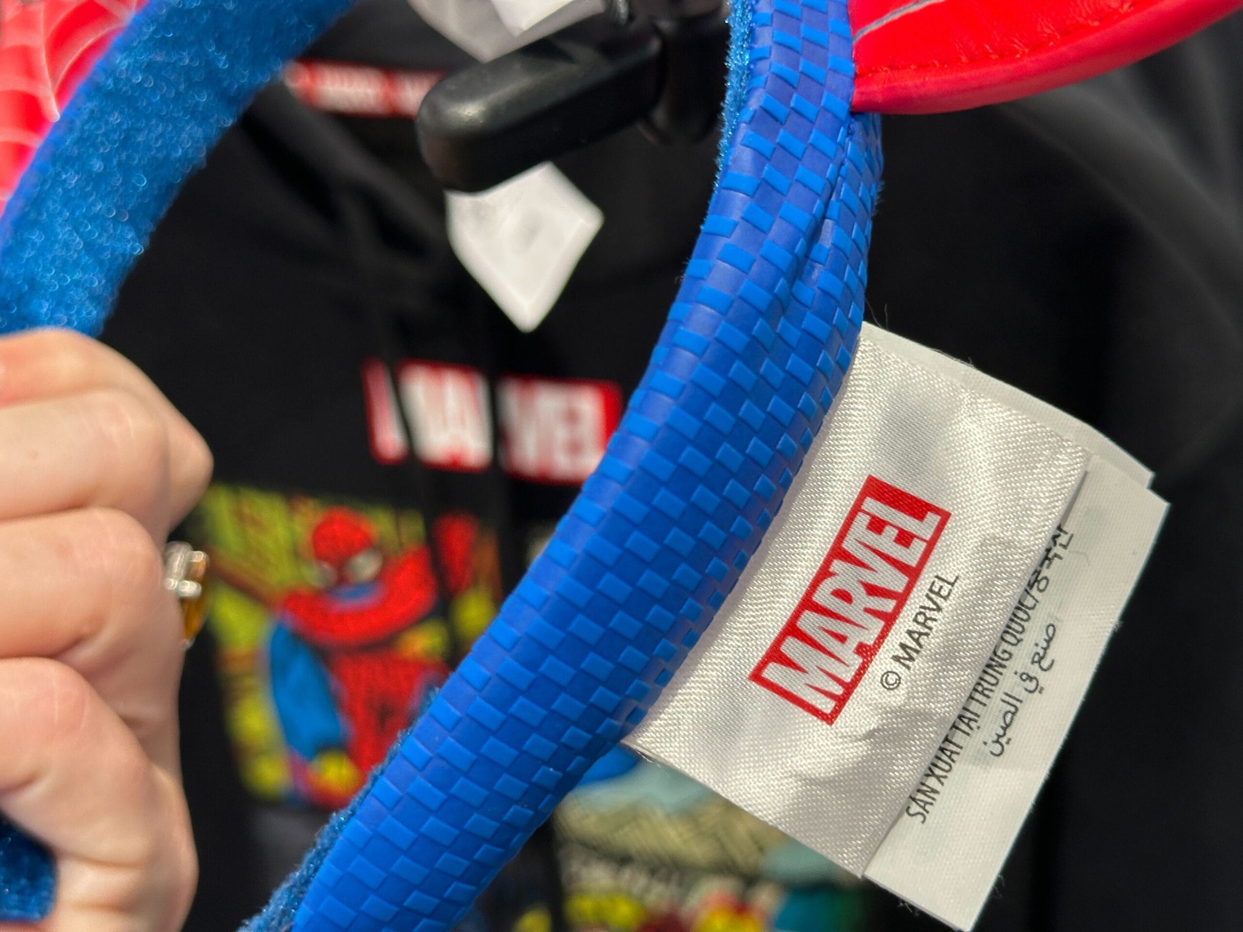A hand holds blue Marvel merchandise with a Marvel tag; a colorful Fantastic Four apparel hoodie is in the background.