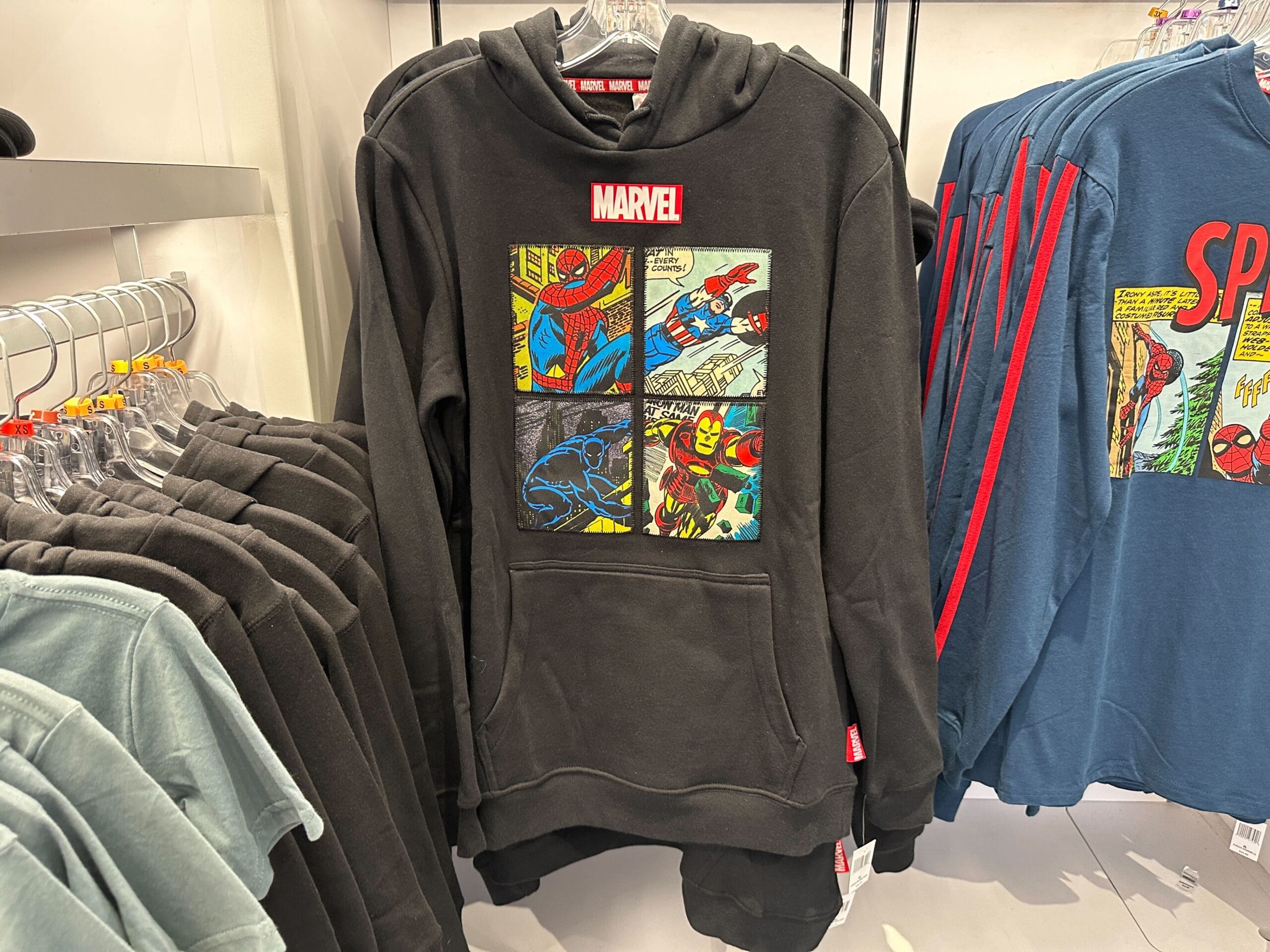 Black Marvel Merchandise hoodie with comic panels of Spider-Man, Iron Man, and Black Panther displayed on a store rack.