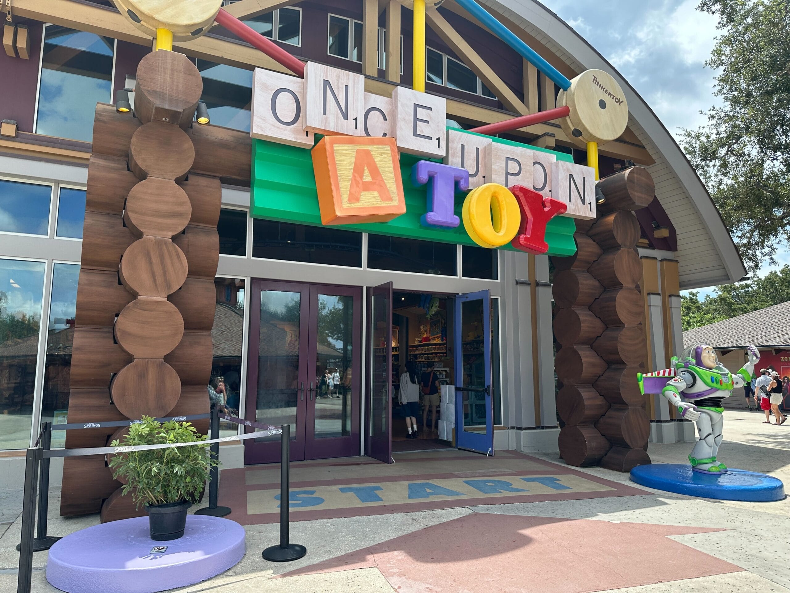 Entrance of "Once Upon a Toy" store with colorful block letters and a Buzz Lightyear statue outside.