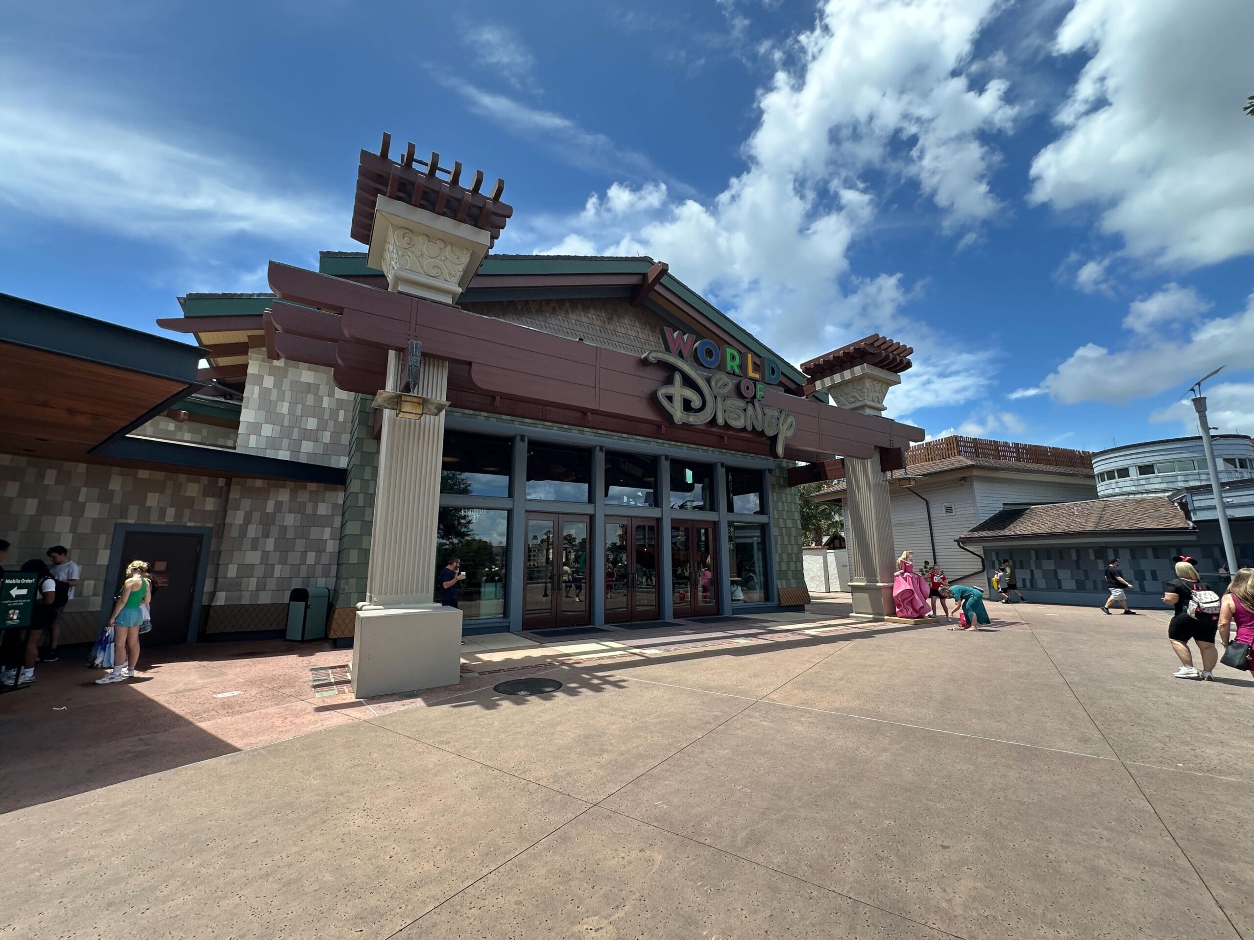 The World of Disney store exterior at Disney Springs on a sunny day, with people and the Cinderella Statue nearby.