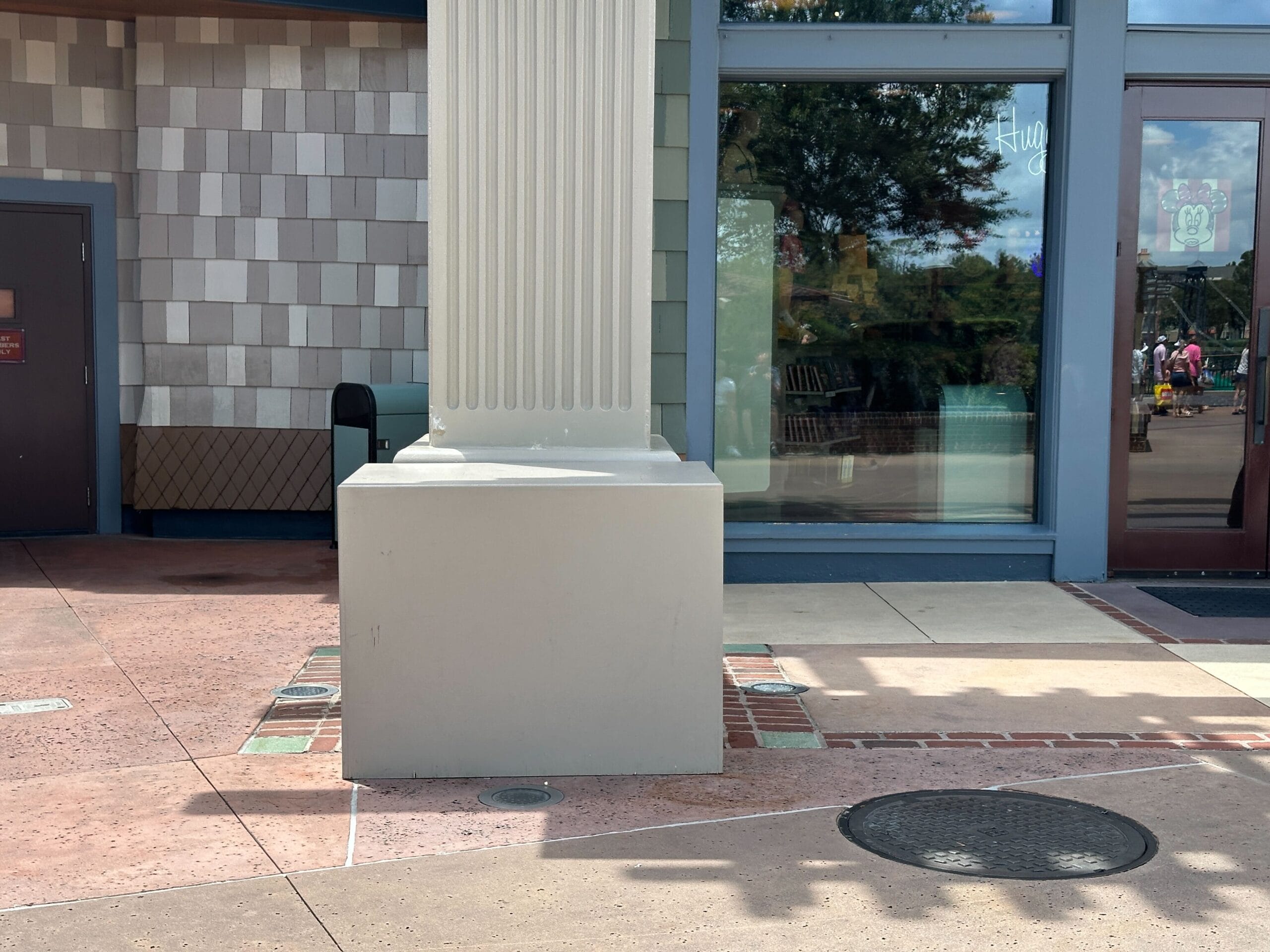 A large square column base sits on a sidewalk near tile walls and windows, awaiting refurbishment at Disney Springs.