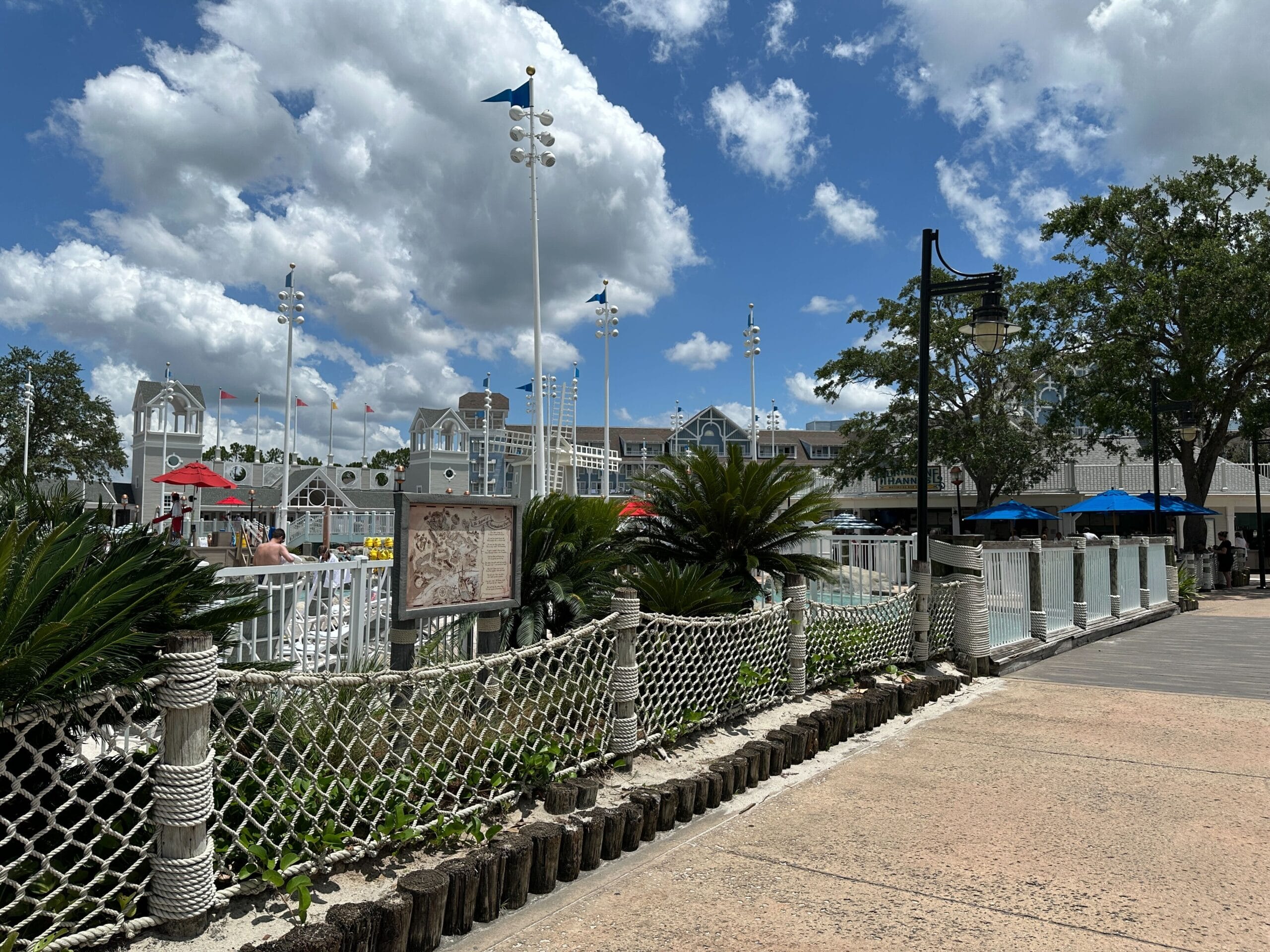 A sunny day at Stormalong Bay, with people swimming at Disney's Yacht Club, palm trees, and a blue sky.