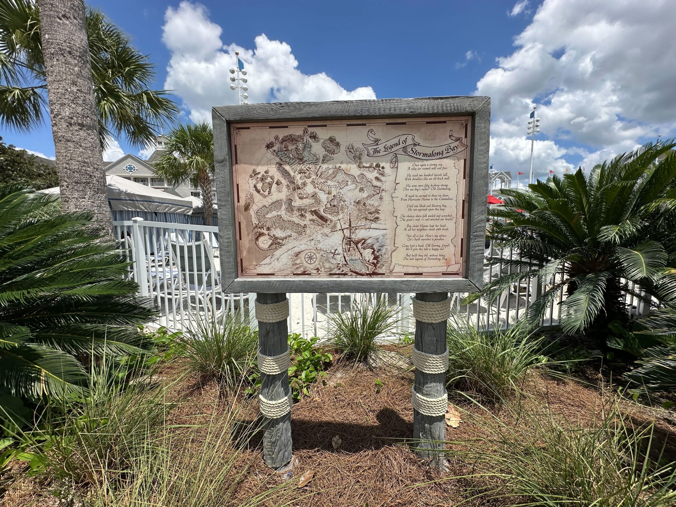 A new Stormalong Bay themed map stands among palm trees near Disney's Yacht Club and Stormalong Bay under a partly cloudy sky.