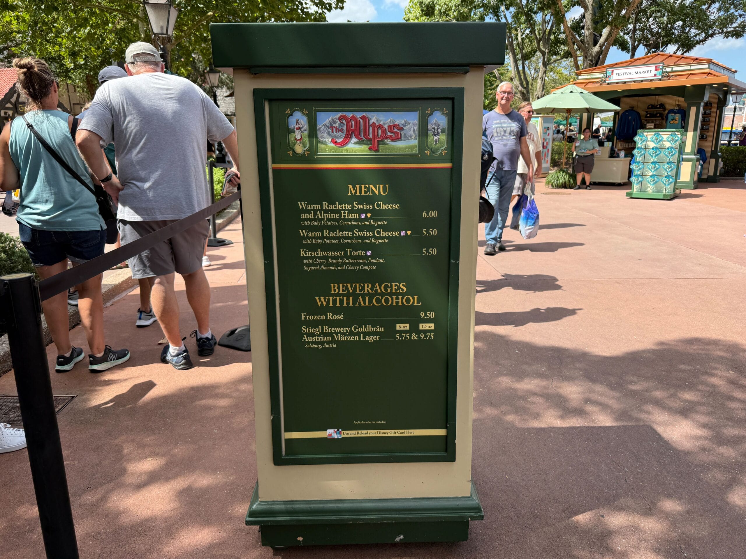 Green Alps Food & Wine booth menu sign with options, people and trees in the background at an outdoor event.