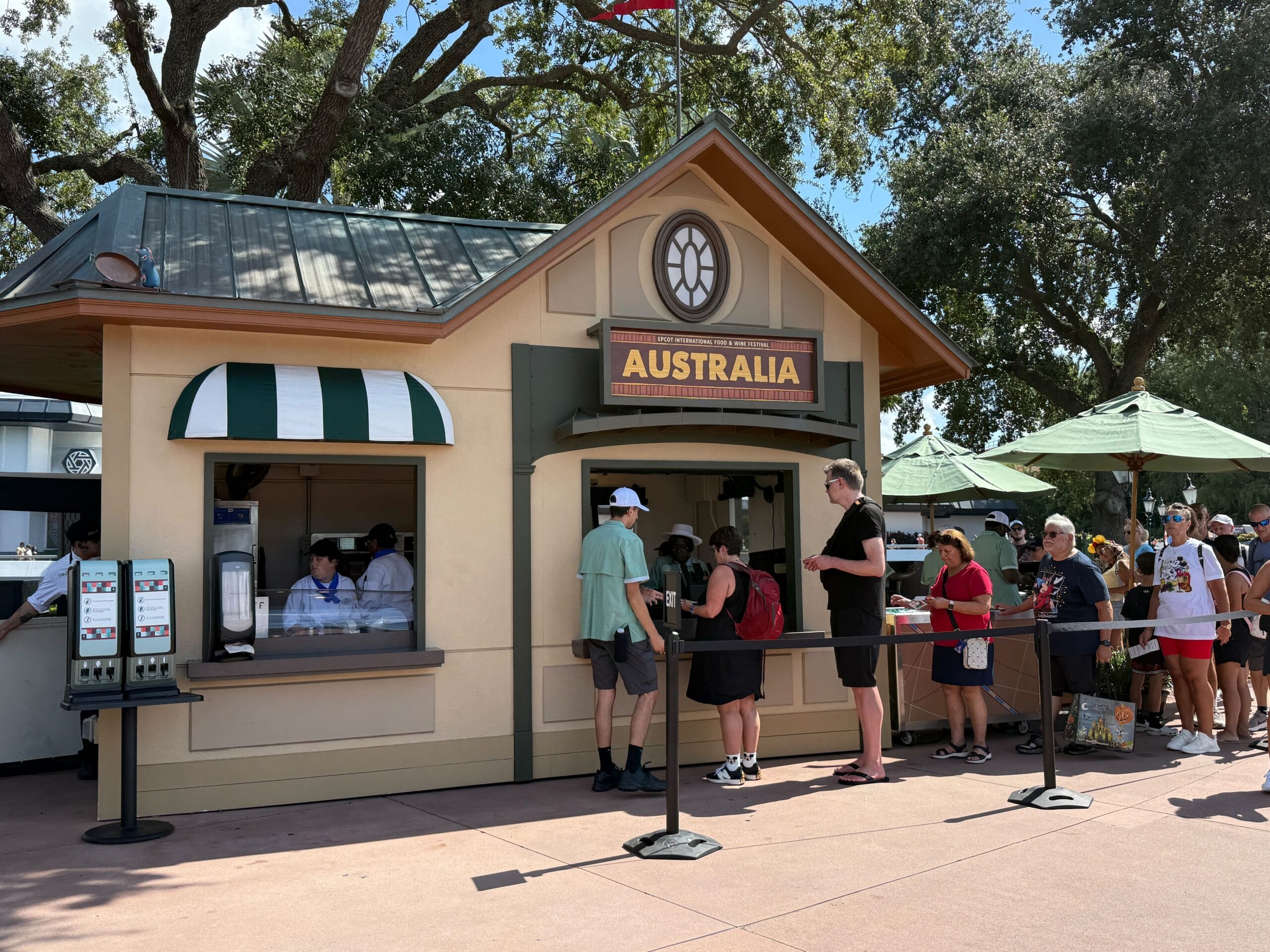 People wait in line at an "Australia" Food & Wine kiosk with a green roof and trees in the background.