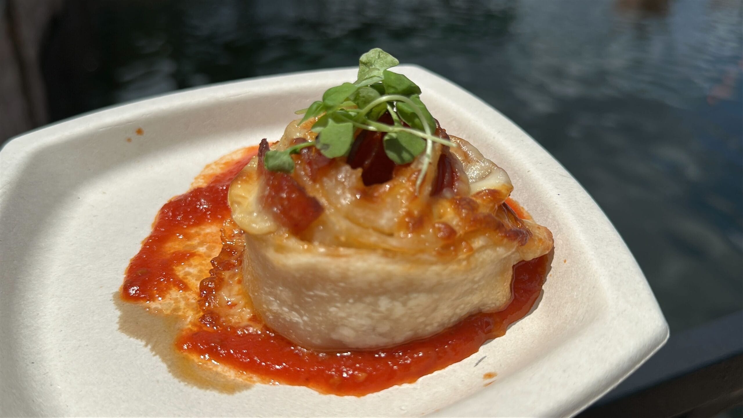 A New Food & Wine favorite: a savory pastry with cheese, bacon, and microgreens atop tomato sauce in a white dish.