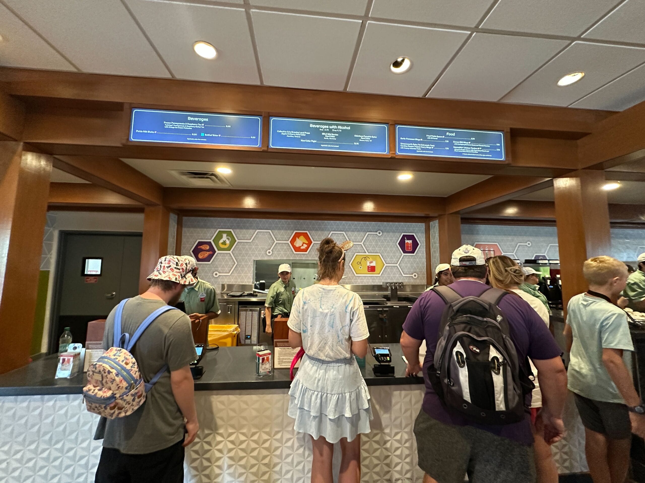 People stand in line at a modern Food & Wine counter-service restaurant with vibrant menu boards and colorful wall art.
