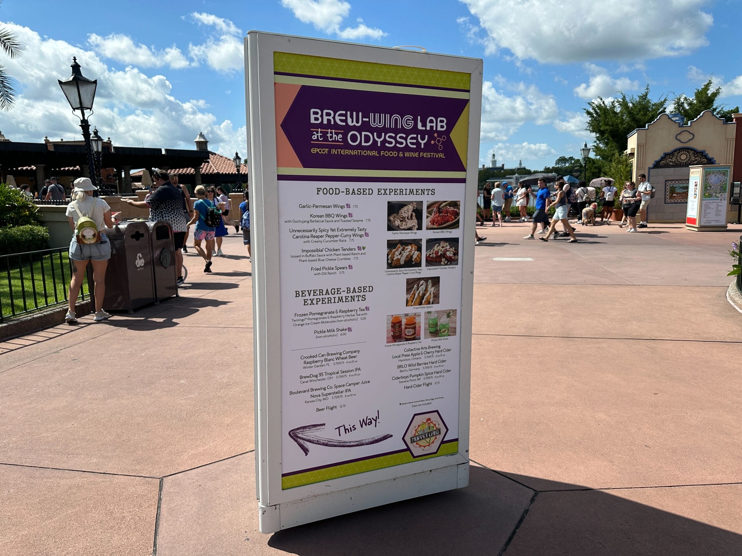 Outdoor sign lists "Brew-Wing Lab at the Odyssey" Food & Wine menu items for the festival; people walk in background.