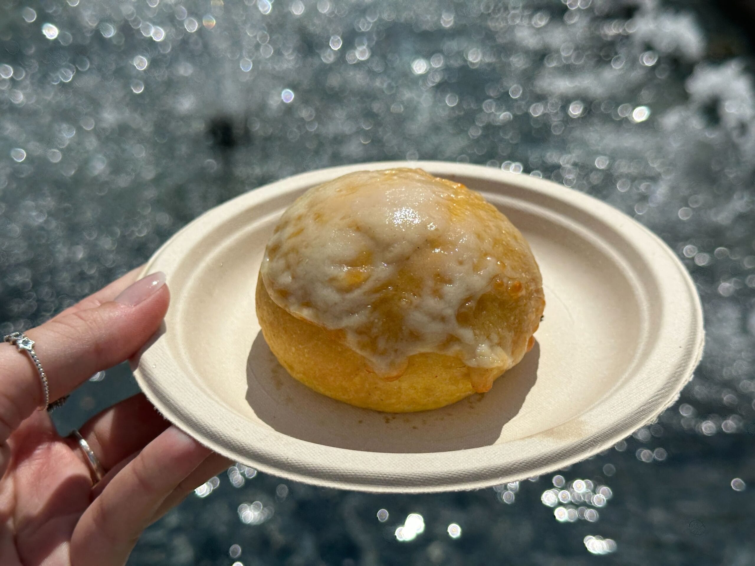A hand holds a plate with a glazed pastry, perfect for enjoying by sparkling water—true Food & Wine moments.