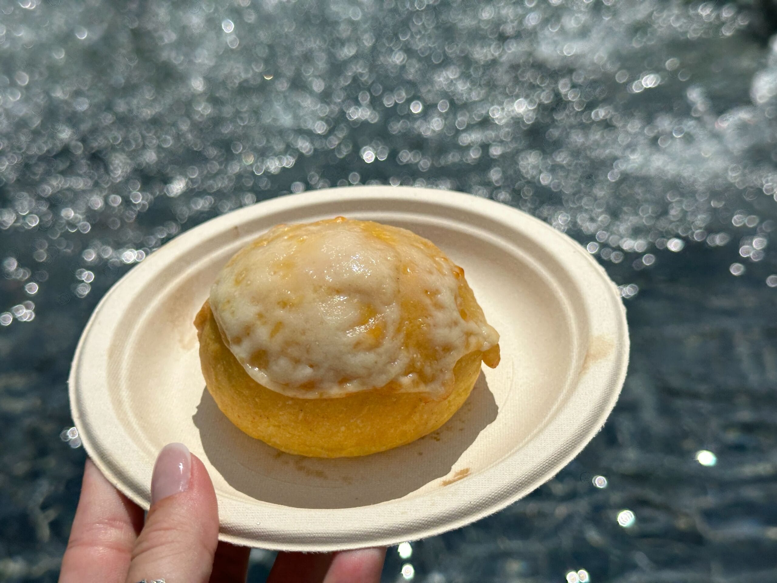 A hand holds a plate with a cheese-covered pastry, perfect for enjoying by sparkling water—true Food & Wine delight.