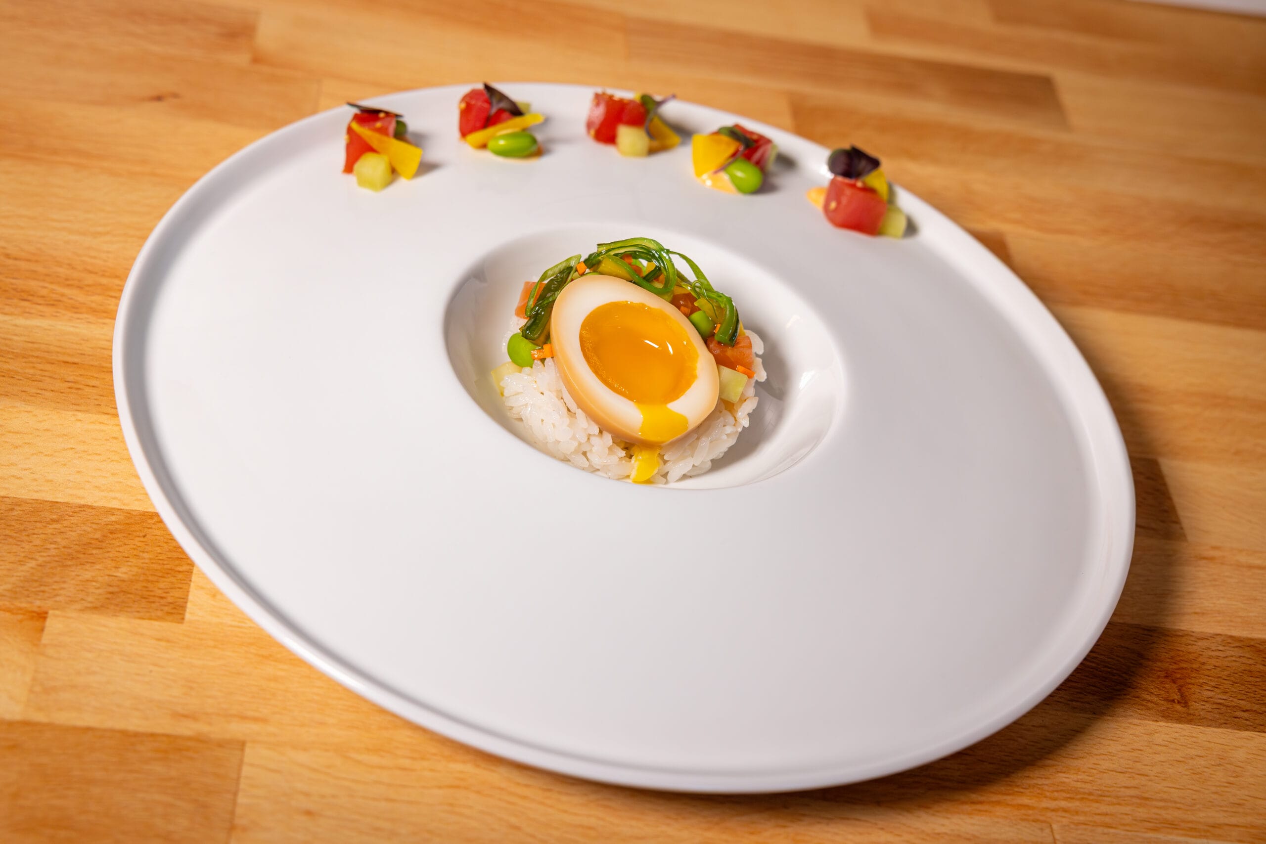 A soft-boiled egg on rice with garnish, plated at Swan and Dolphin, features colorful veggies on a large white dish.