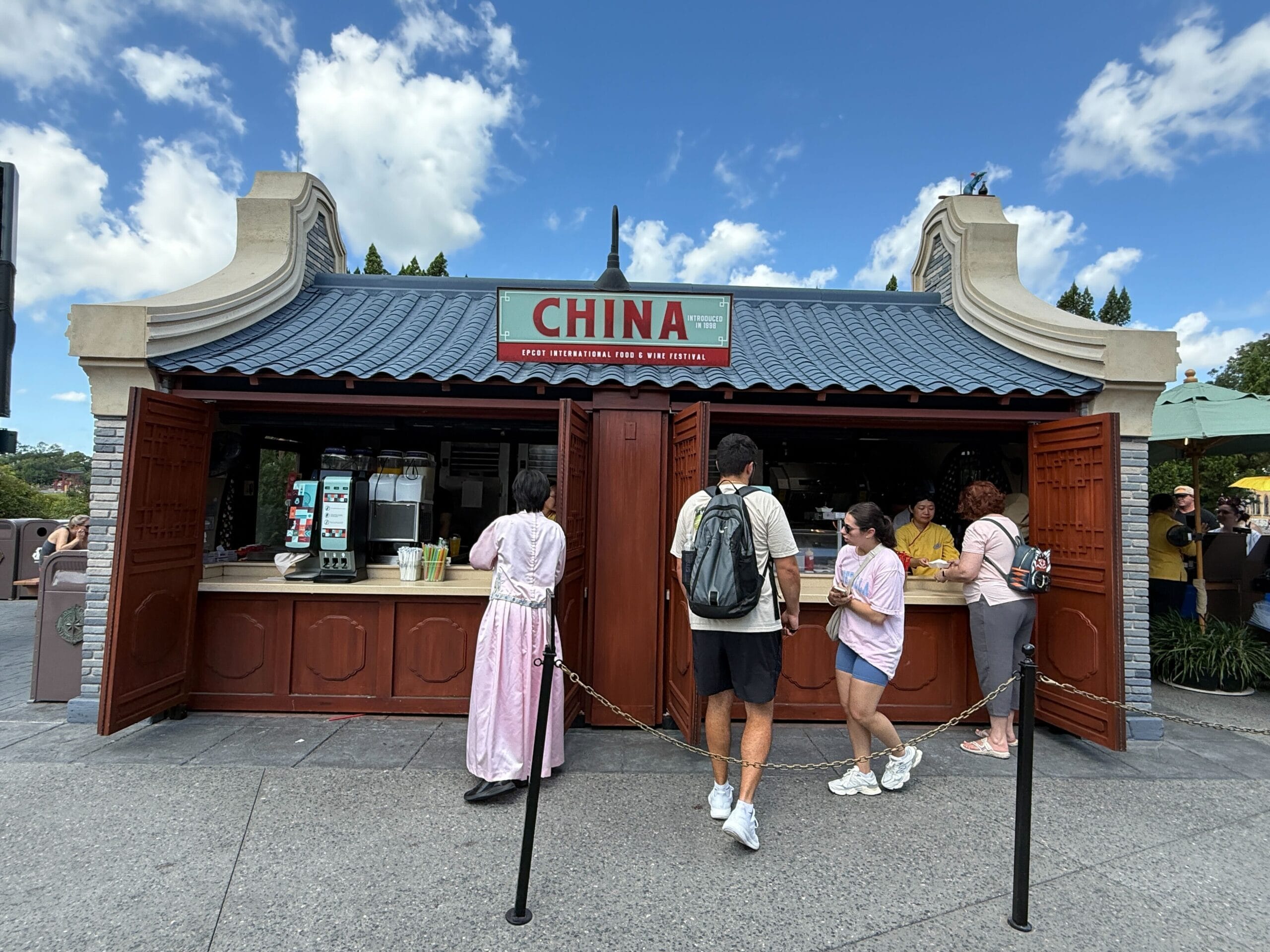 Outdoor Food & Wine booth labeled "China," with people ordering at the counter under a blue, cloud-filled sky.