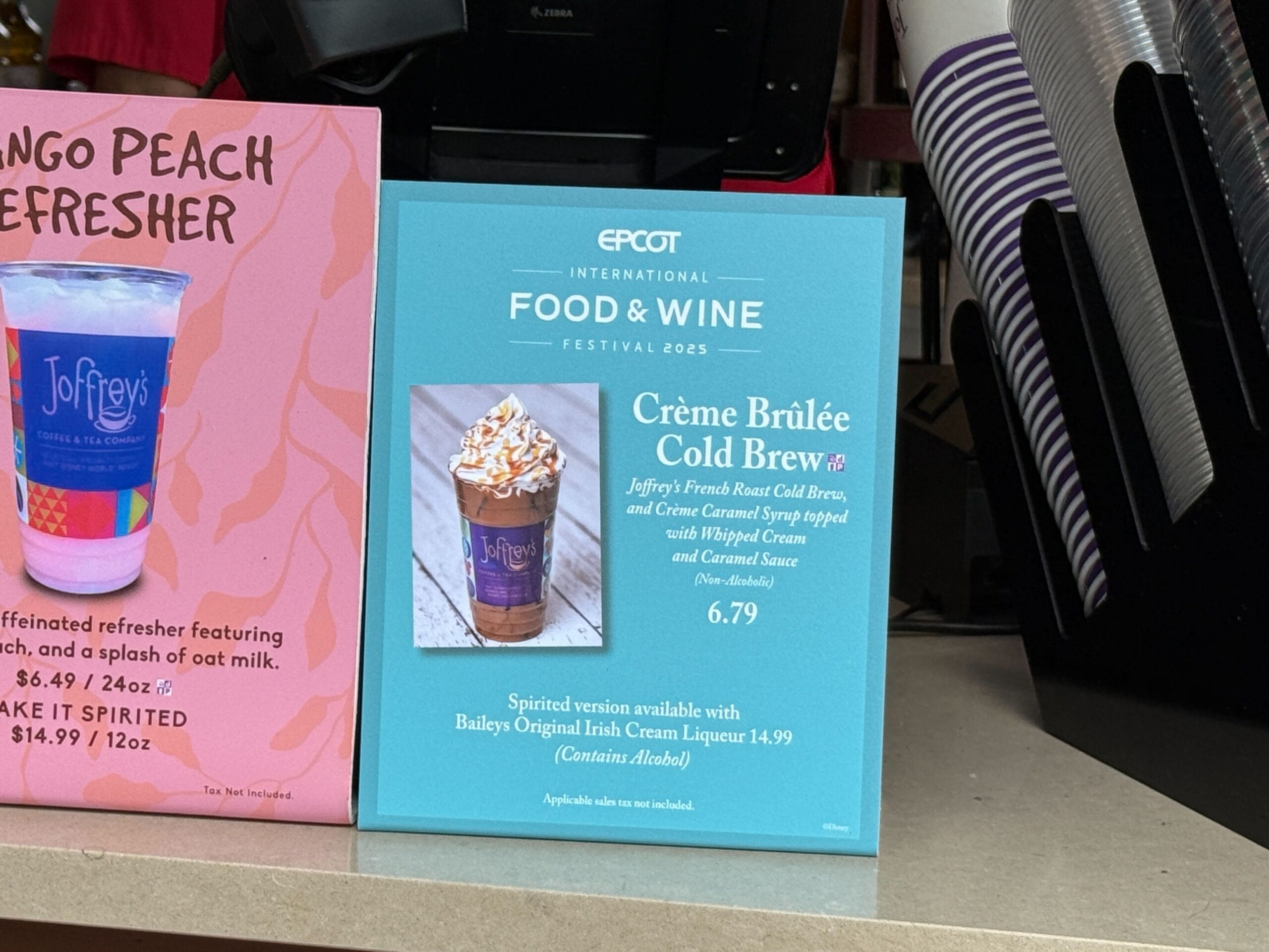 A sign showcases New Food & Wine Crème Brûlée Cold Brew details and price beside a mango drink menu at Epcot.