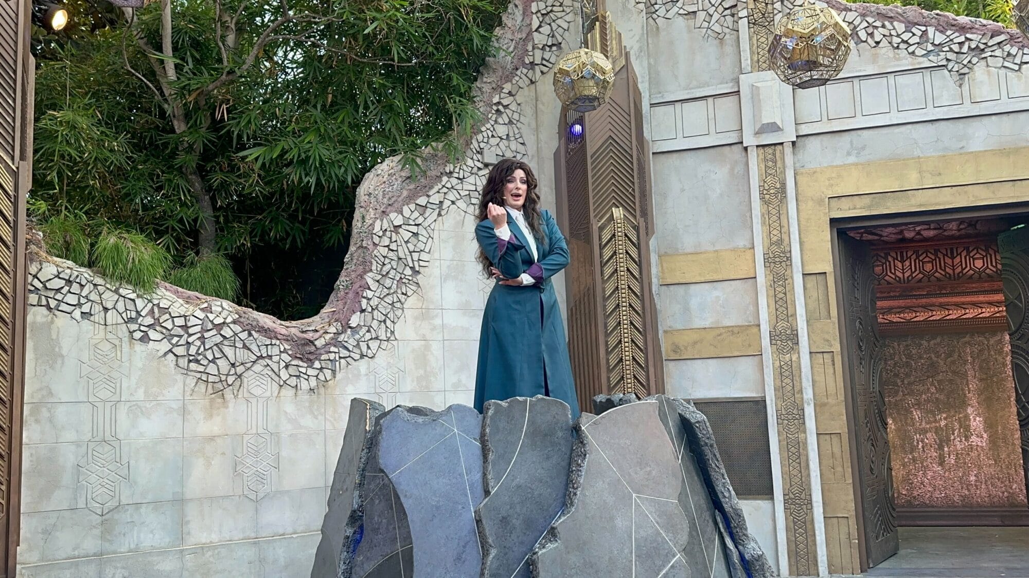 A woman in a teal coat performs on a rocky stage with mosaic walls at Oogie Boogie Bash, Disney California Adventure 2025.