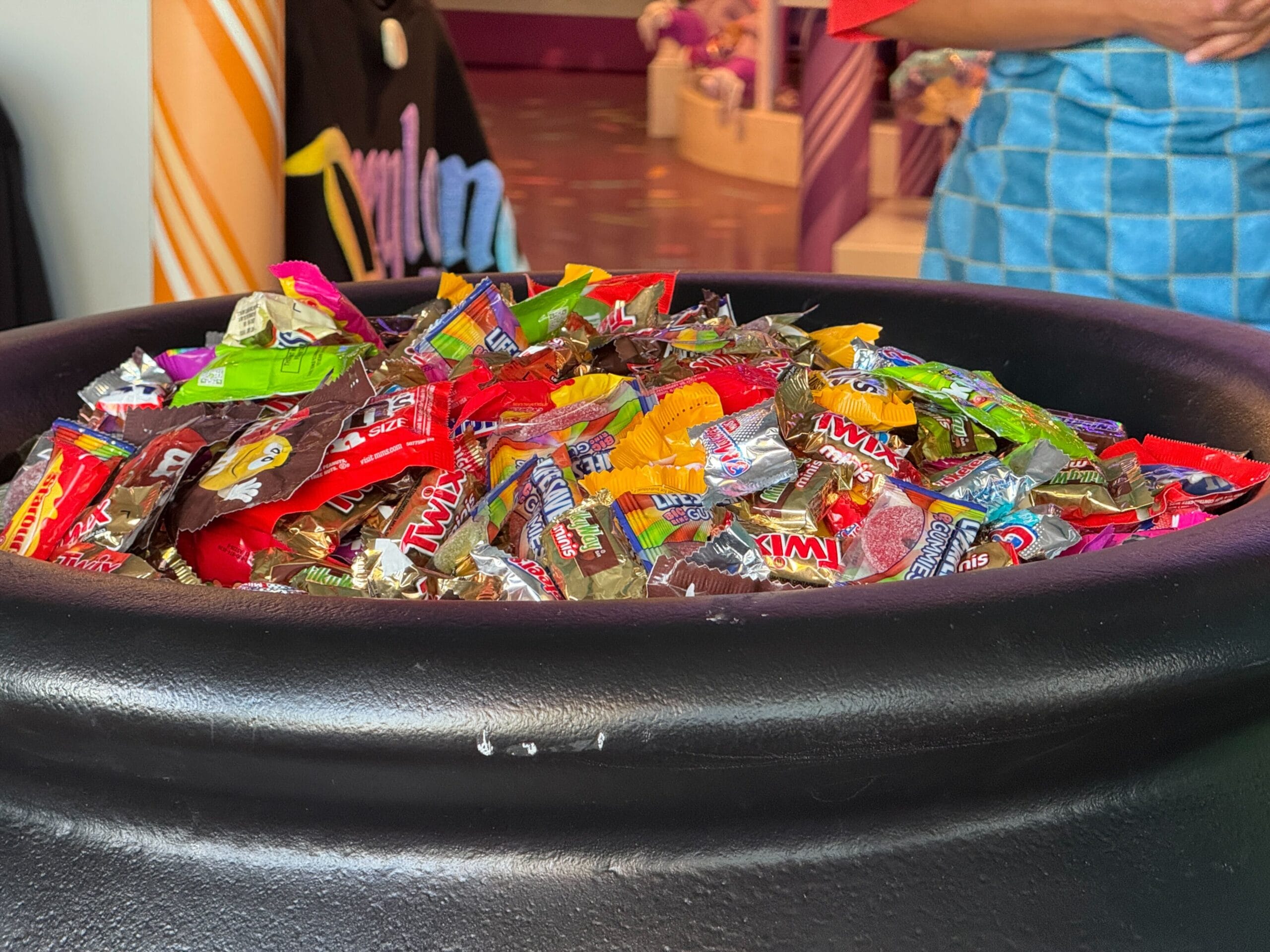 A large black cauldron filled with assorted wrapped candies at a Disney Oogie Boogie Bash Treat Trail location.