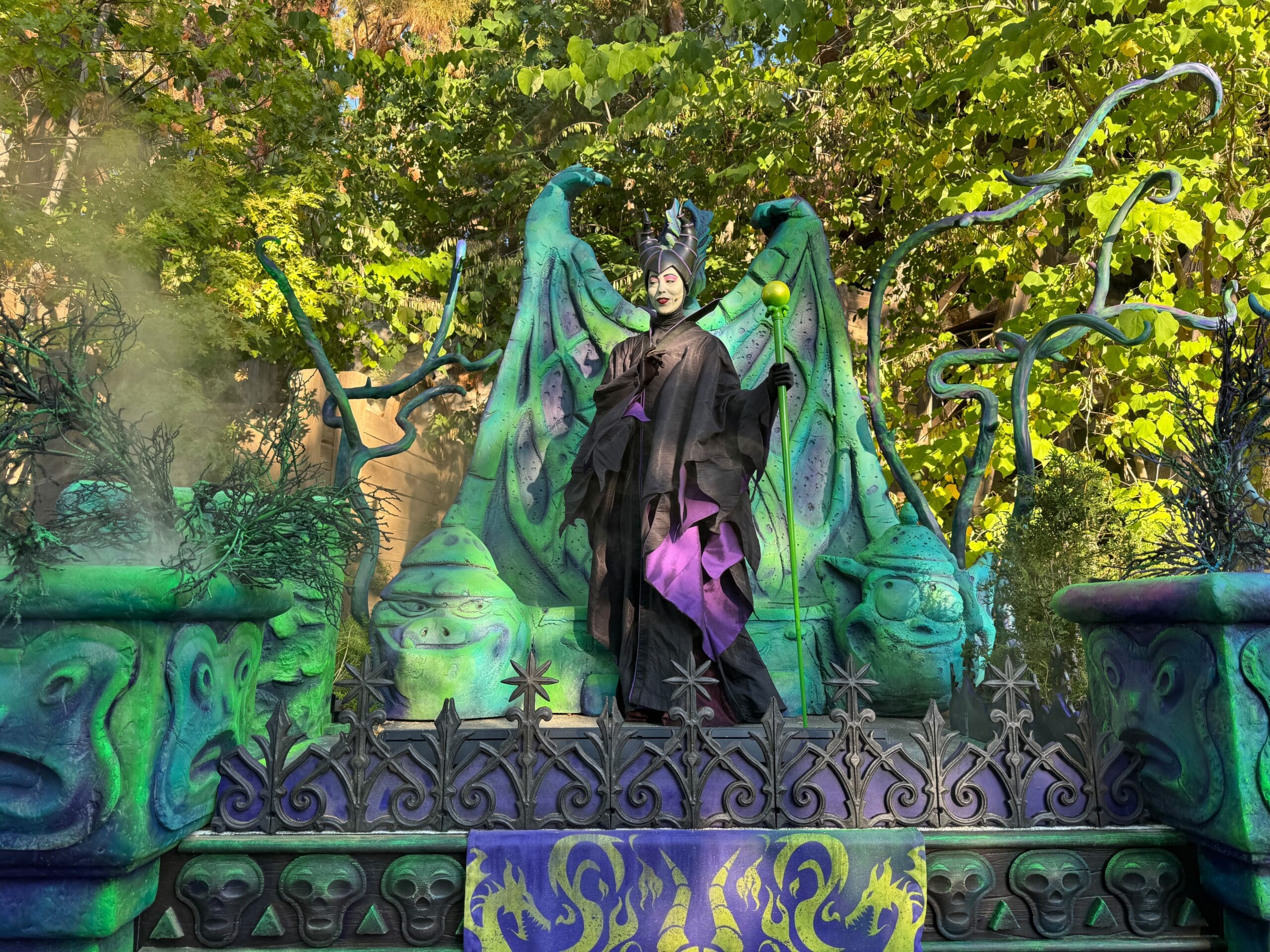 Person in a Maleficent costume stands on a Villains-themed float at Oogie Boogie Bash, surrounded by spooky faces and twisted vines.
