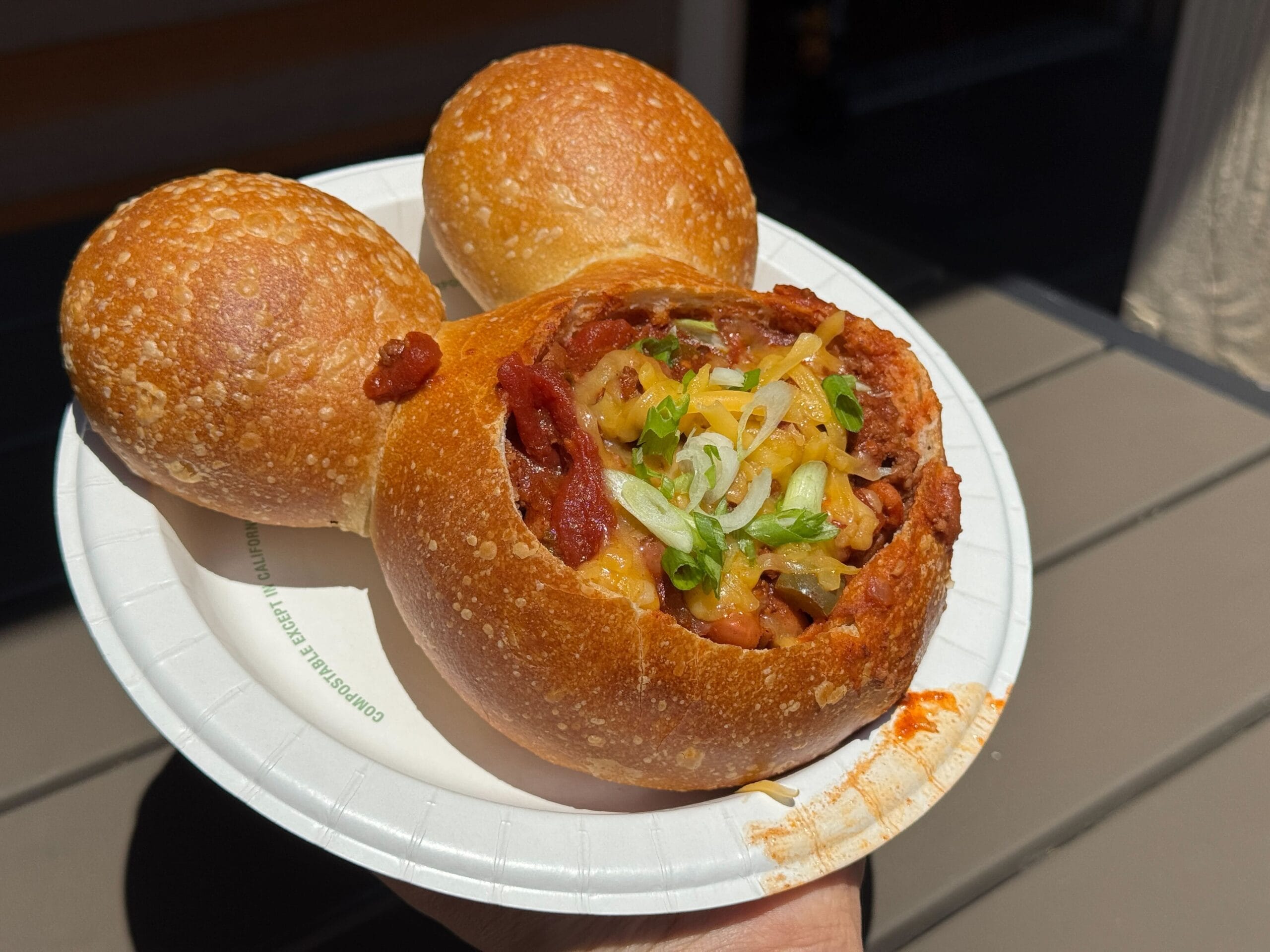 Enjoy Walt's Chili served in a Mickey Shaped Bread Bowl, topped with cheese and green onions on a white plate at Disney.