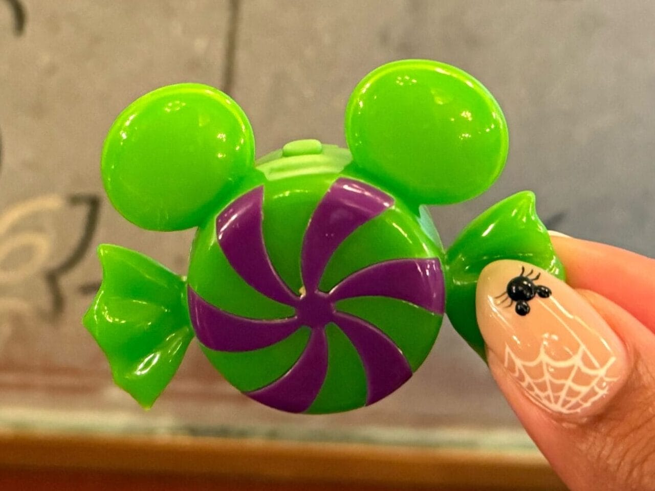 A hand with spider nail art holds Disneyland Halloween candy shaped like Mickey Mouse in front of a mirror.
