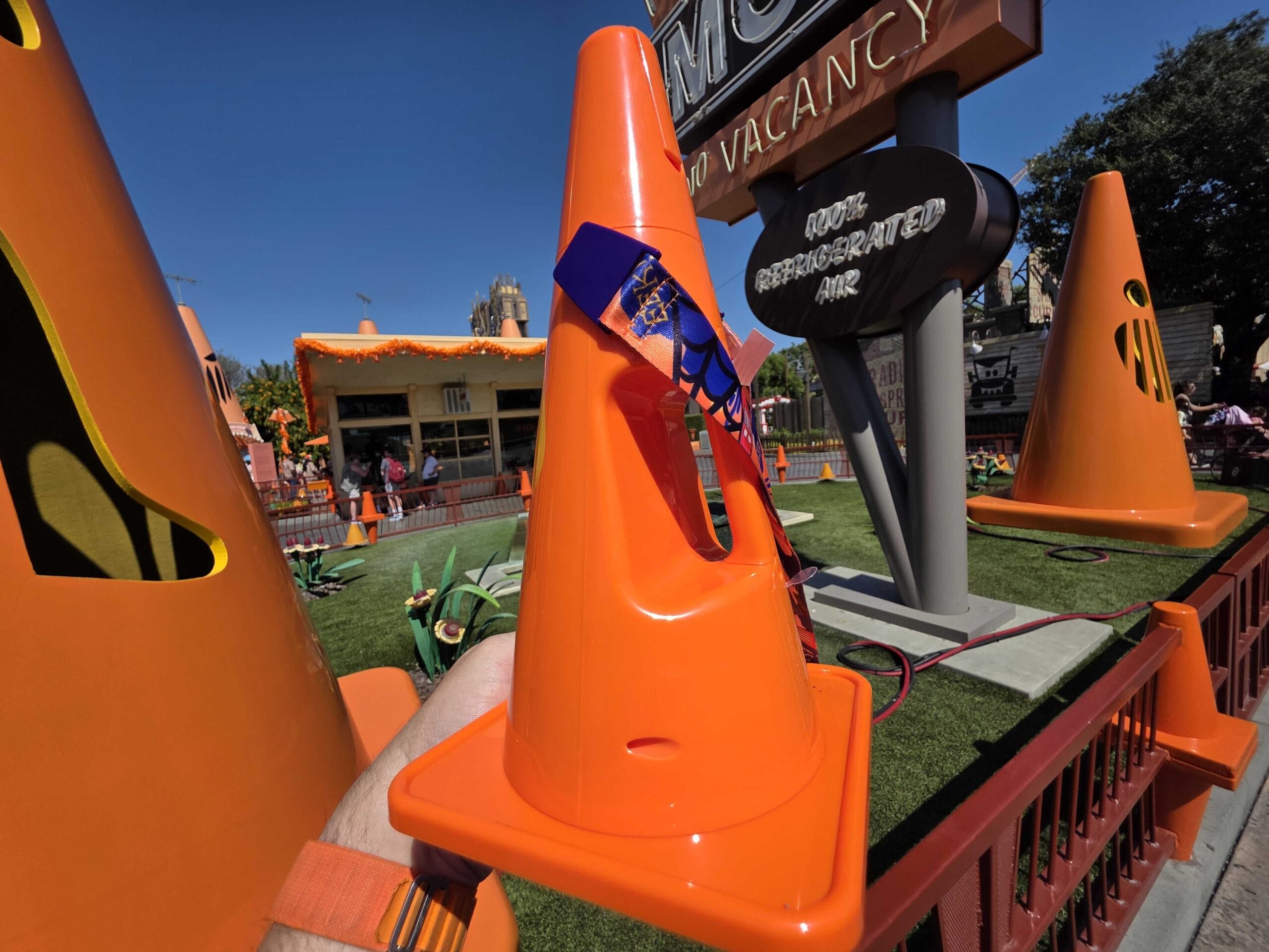 Close-up of bright orange traffic cones in a playful outdoor setting with signs and artificial grass under clear sky.