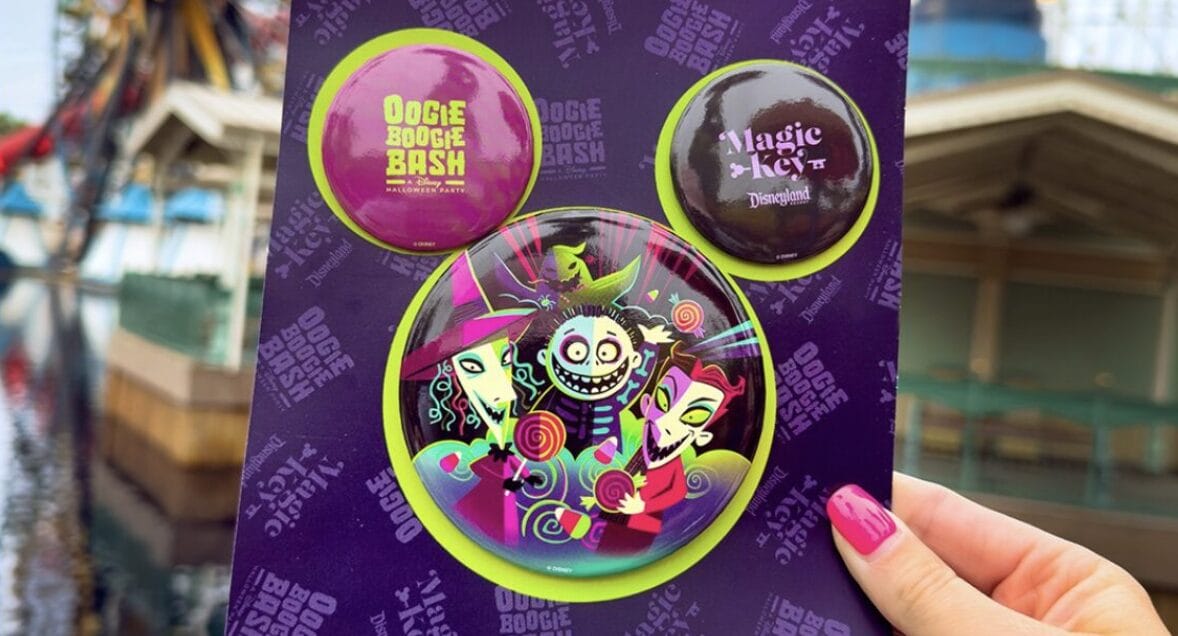 A hand holds OBB Magic Key buttons with vibrant villain art at a lively theme park.