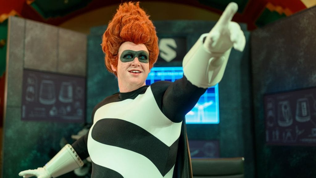 A person in a Syndrome-inspired superhero costume with a red wig poses dramatically at Oogie Boogie Bash 2025.