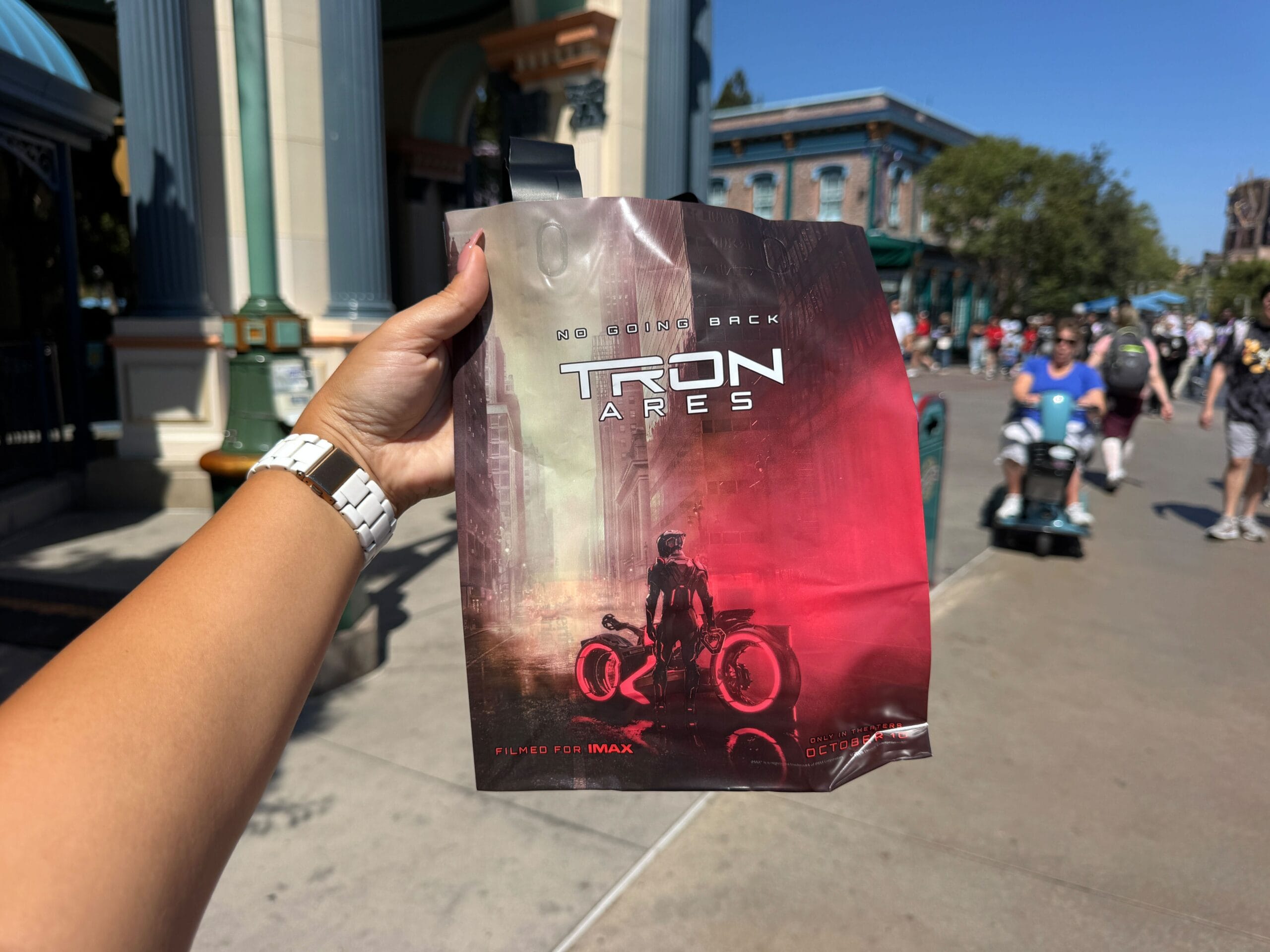 A hand holds a "Tron: Ares" promo bag and an Event Map in a theme park during the 2025 Oogie Boogie Bash.