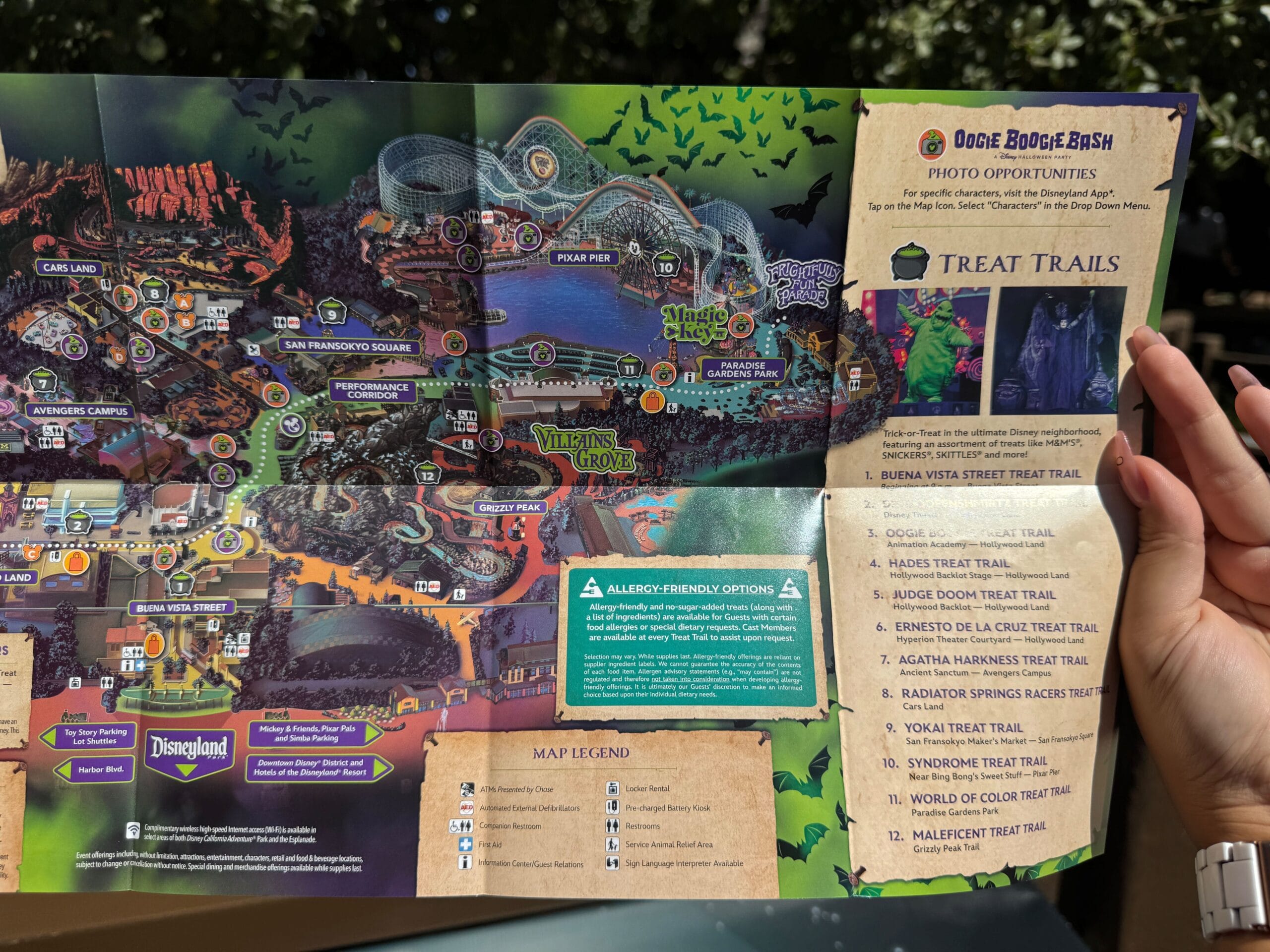 Person holding an Oogie Boogie Bash event map open, showing treat trails, attractions, and special wristband locations.