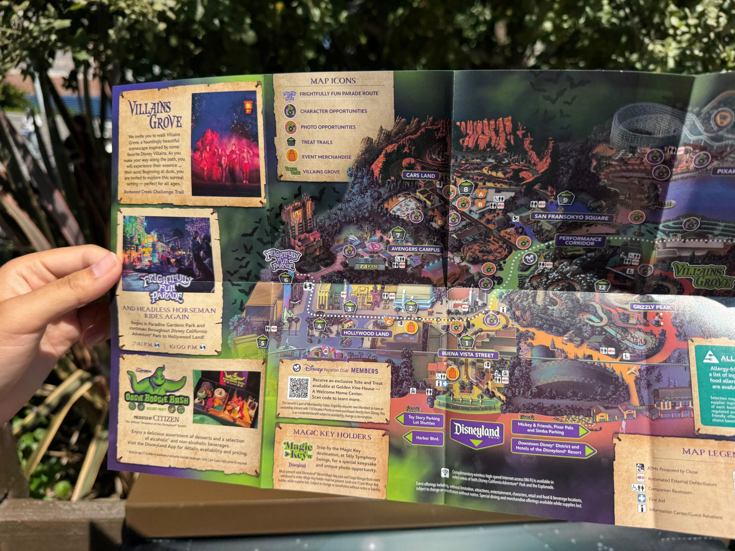 A hand holds a colorful 2025 Oogie Boogie Bash Event Map, showing maps and icons in bright outdoor sunlight.