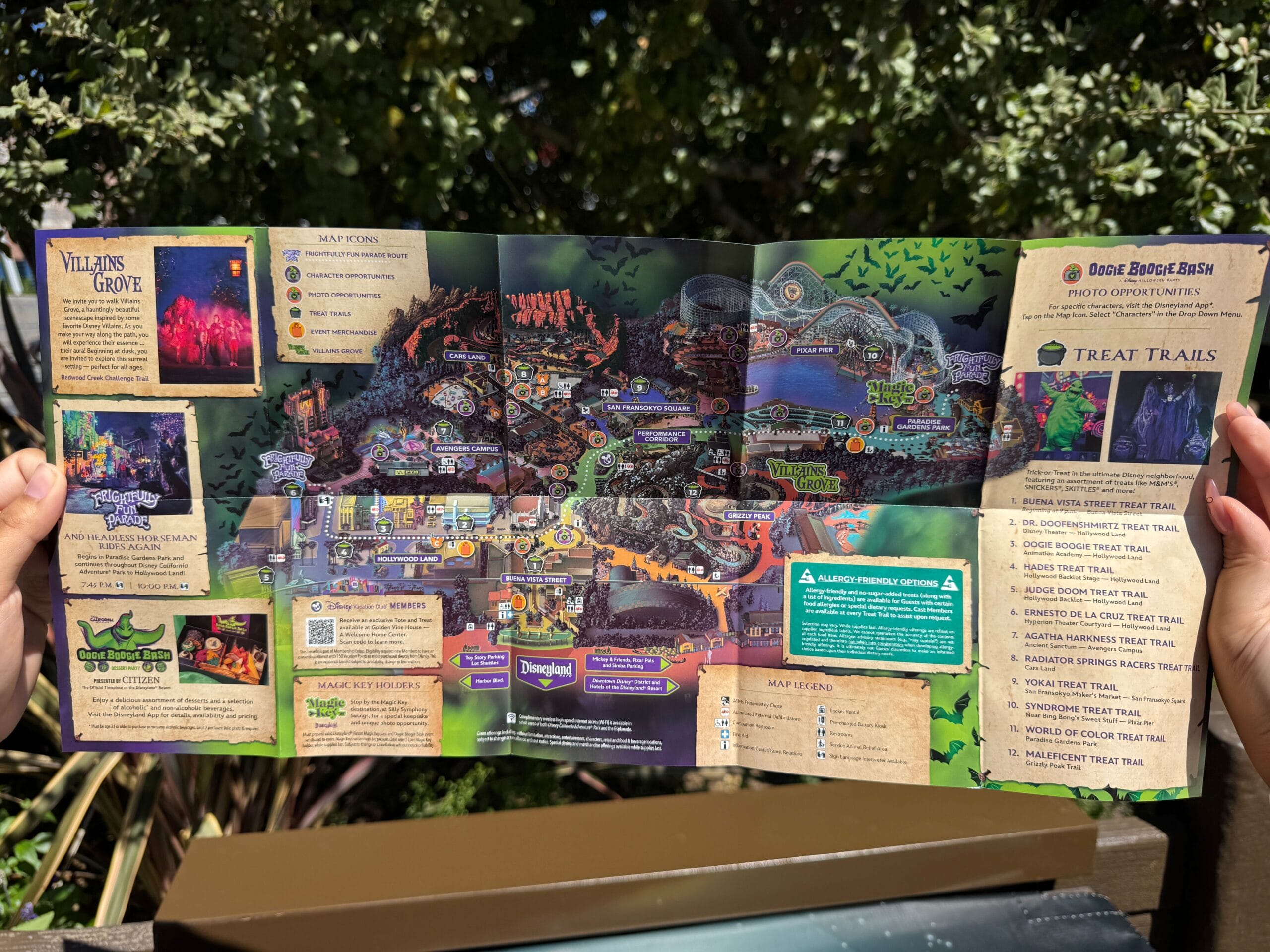 Person holding a 2025 Oogie Boogie Bash Event Map and guide outdoors, with trees in the background.