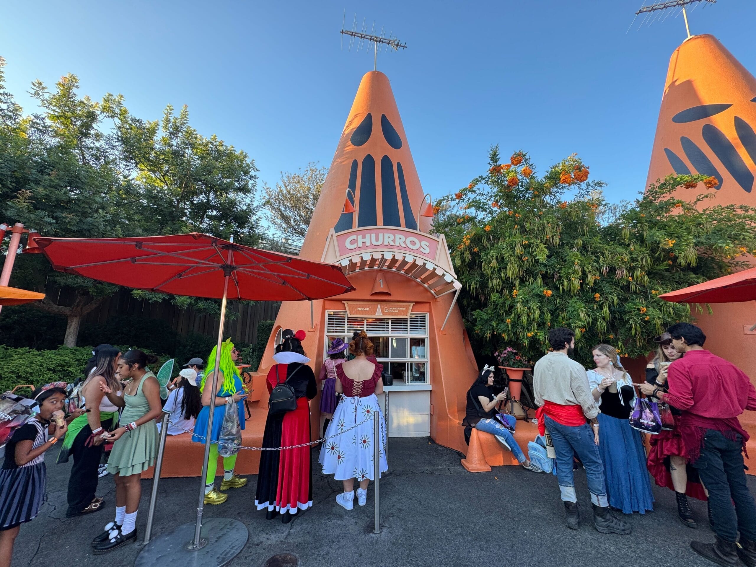 People in costumes line up at the Cozy Cone 1 ordering window at Disney California Adventure, which is decorated for Halloween.