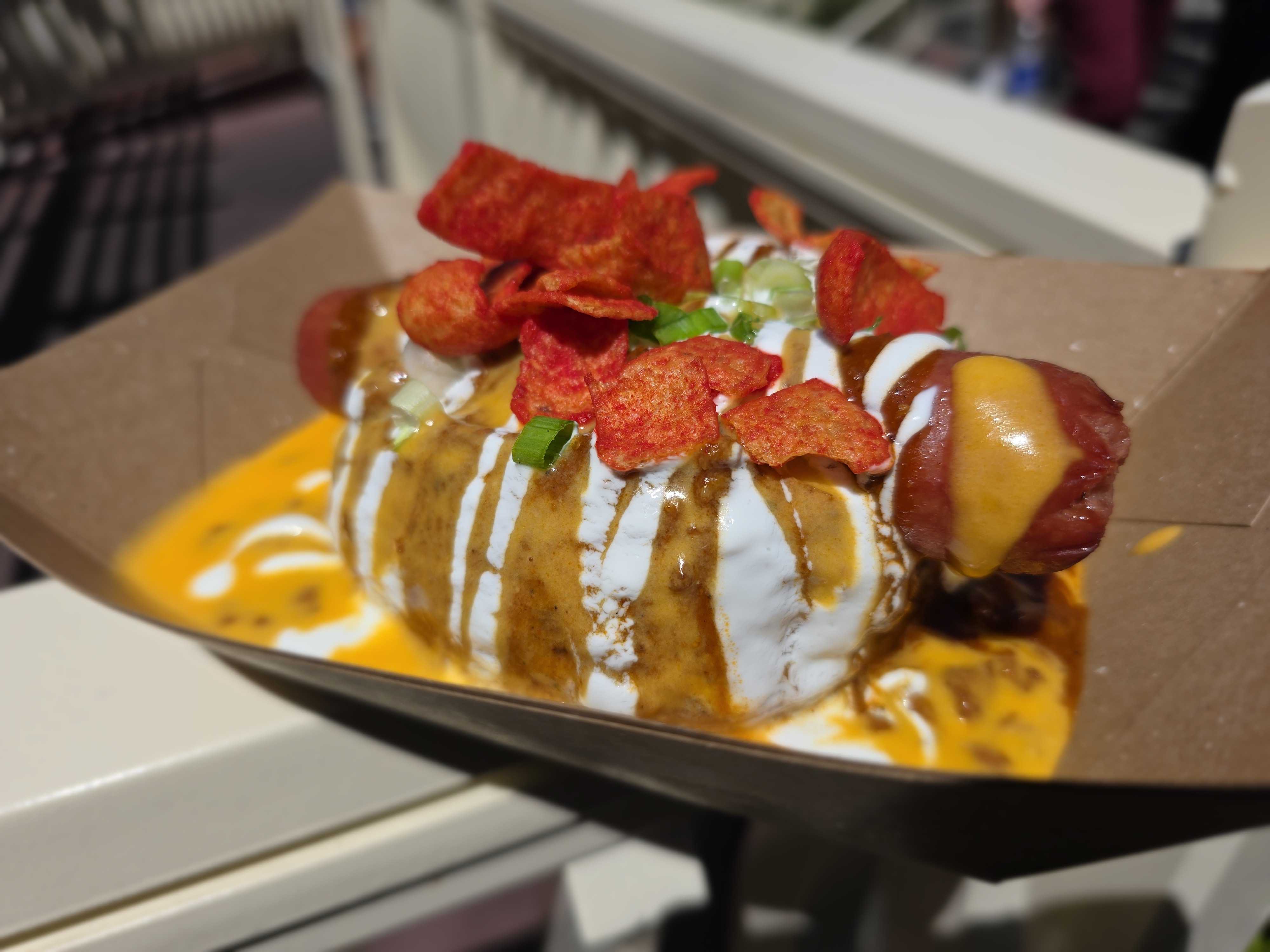 A Refreshment Corner hot dog topped with cheese sauce, sour cream, green onions, and red tortilla chips at Disneyland.