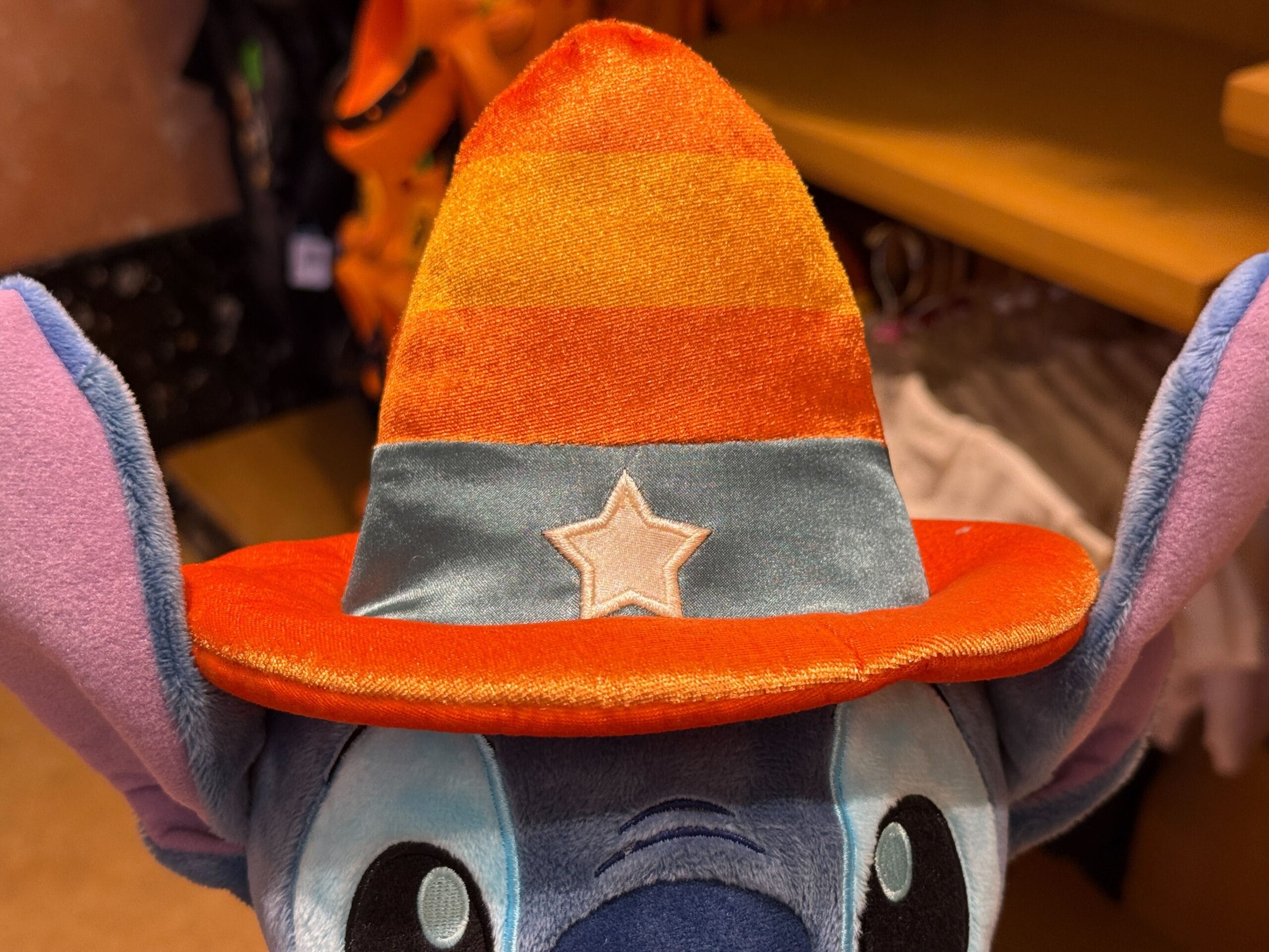 Blue plush toy wearing an orange striped wizard hat with a white star, spotted among Disneyland Halloween merchandise.