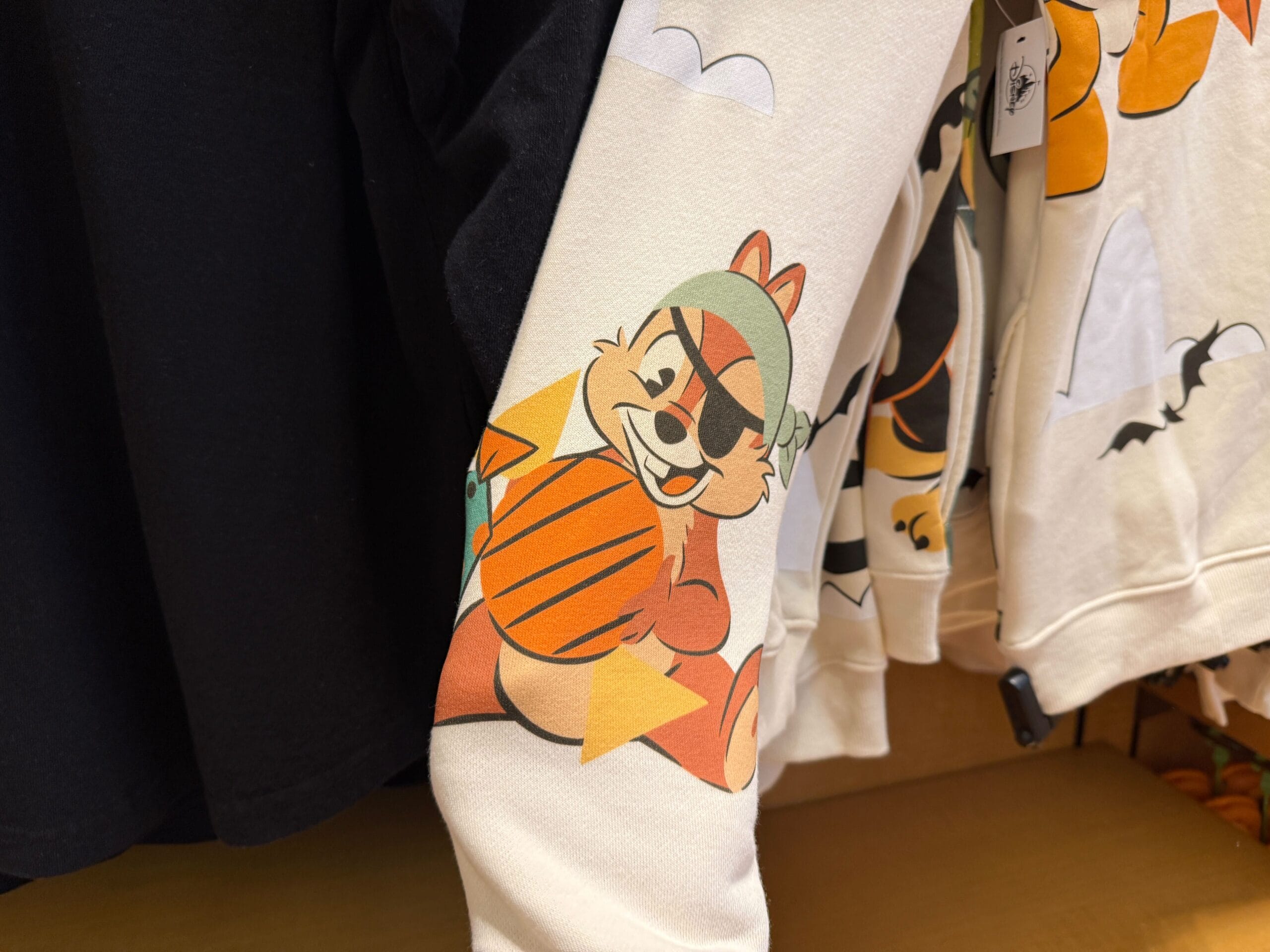 Cartoon chipmunk with eyepatch and pumpkin, perfect Halloween merchandise on a cream-colored sweatshirt sleeve.