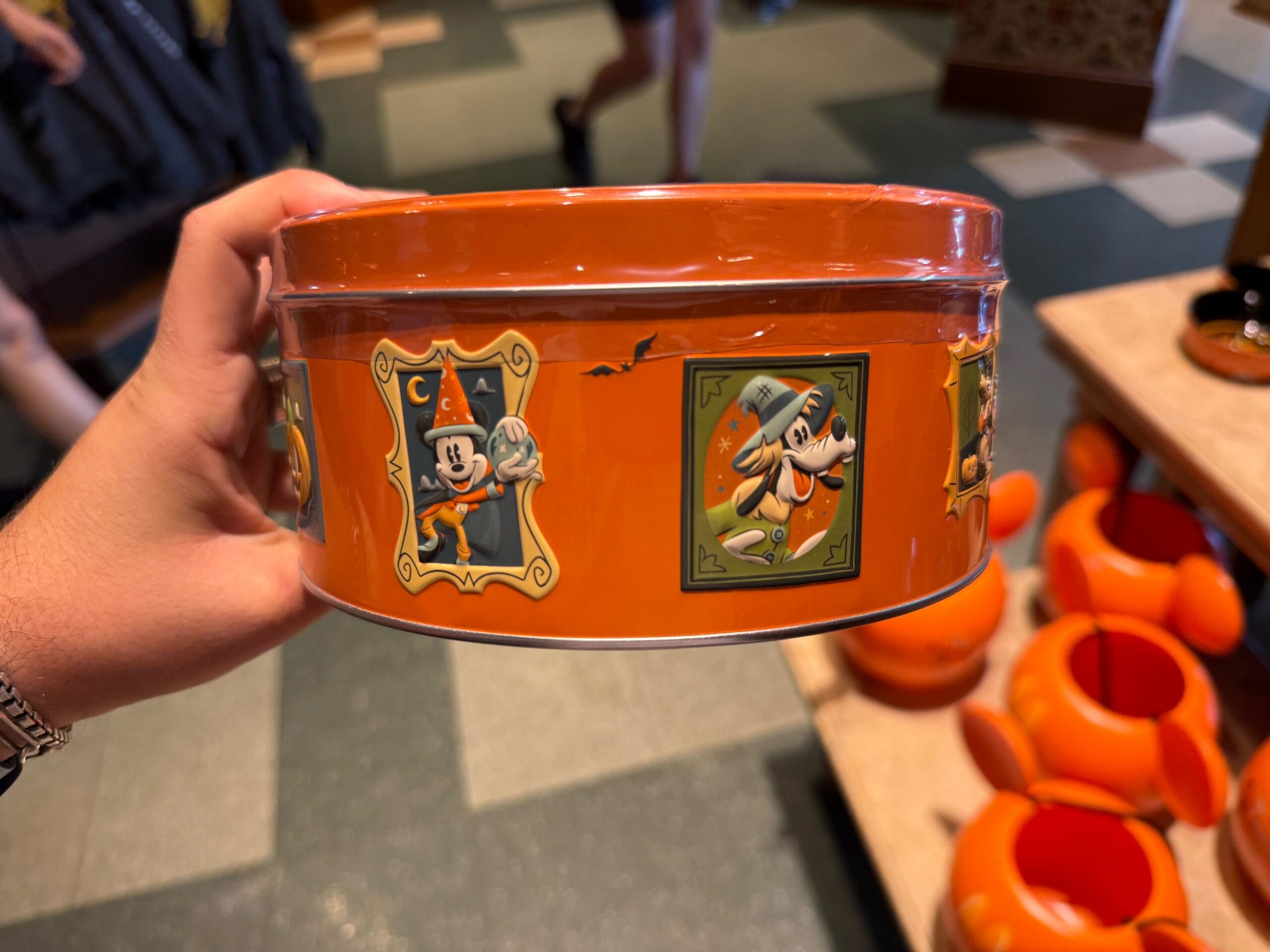 An orange tin featuring Halloween Merchandise with Mickey and Pluto, spotted at Disneyland among pumpkin-shaped items.