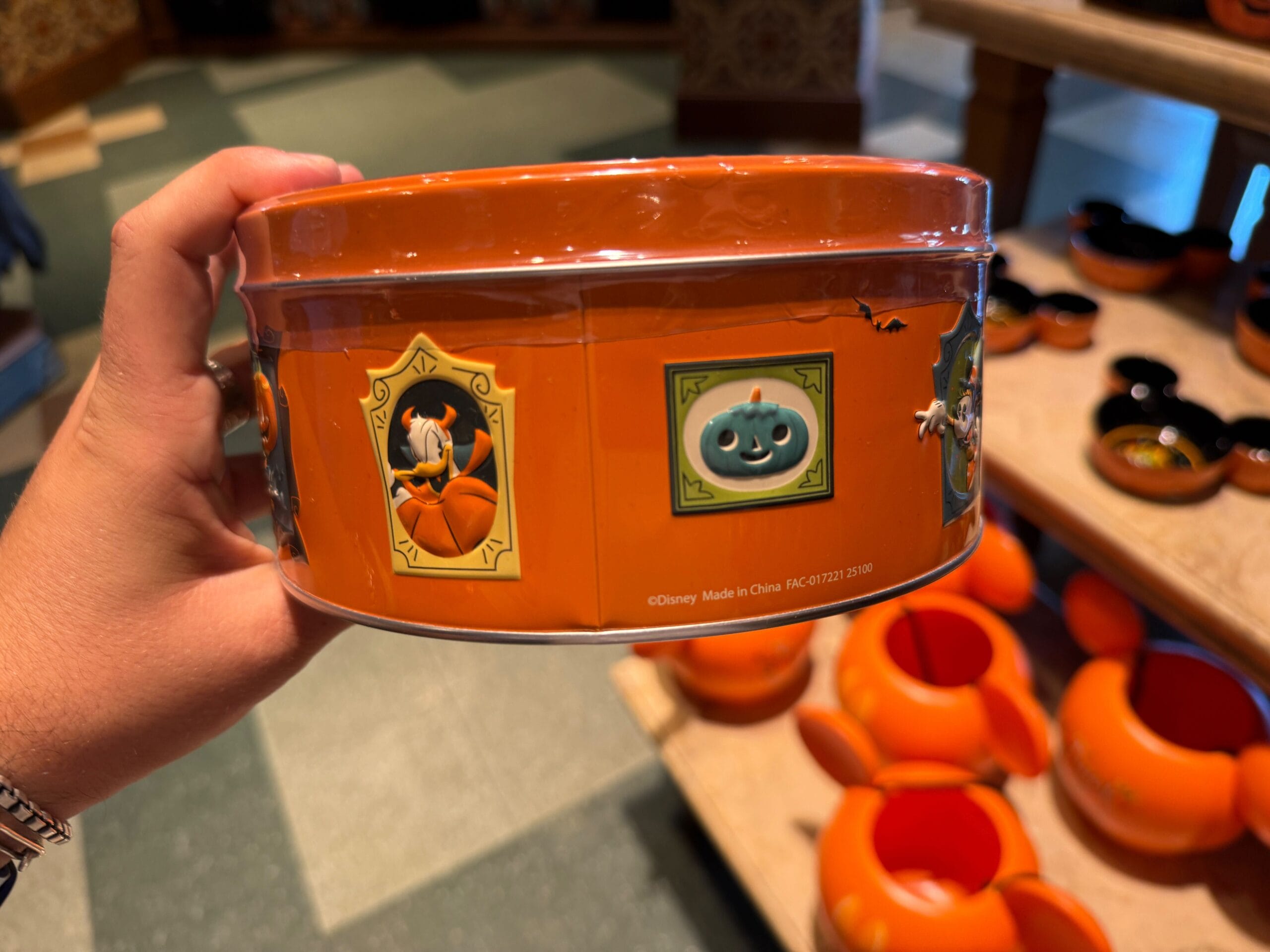 Hand holding Halloween Disney merchandise tin; pumpkin-shaped bowls in background, perfect for Disneyland fans.