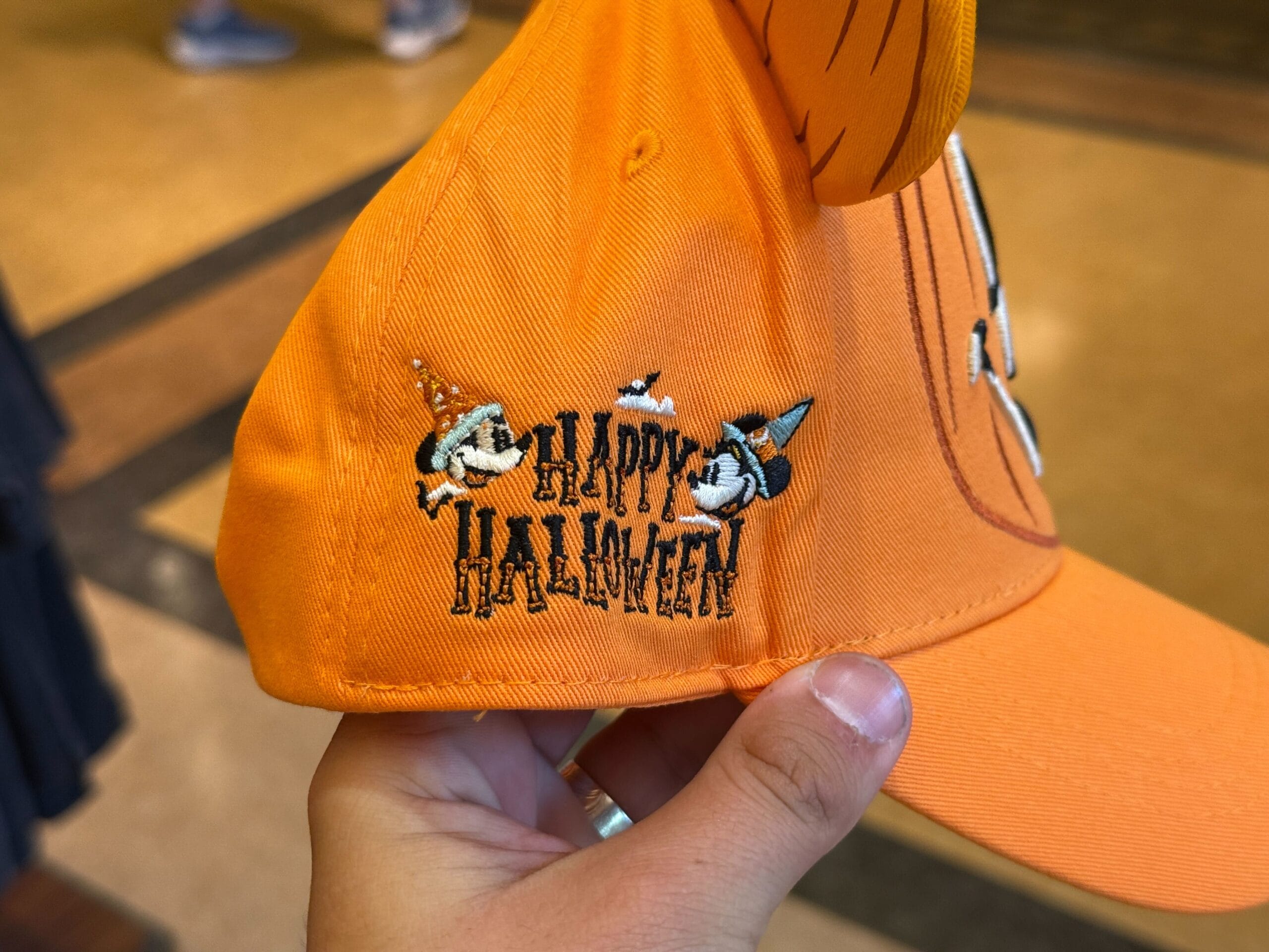 An orange Halloween merchandise hat with "Happy Halloween" and two Disney-style witches embroidered on the side.