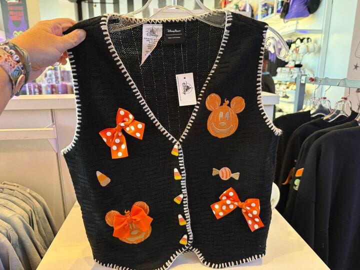 A black vest with orange Mickey Mouse faces, bows, candy decorations—perfect Pumpkin Apparel displayed in a store.