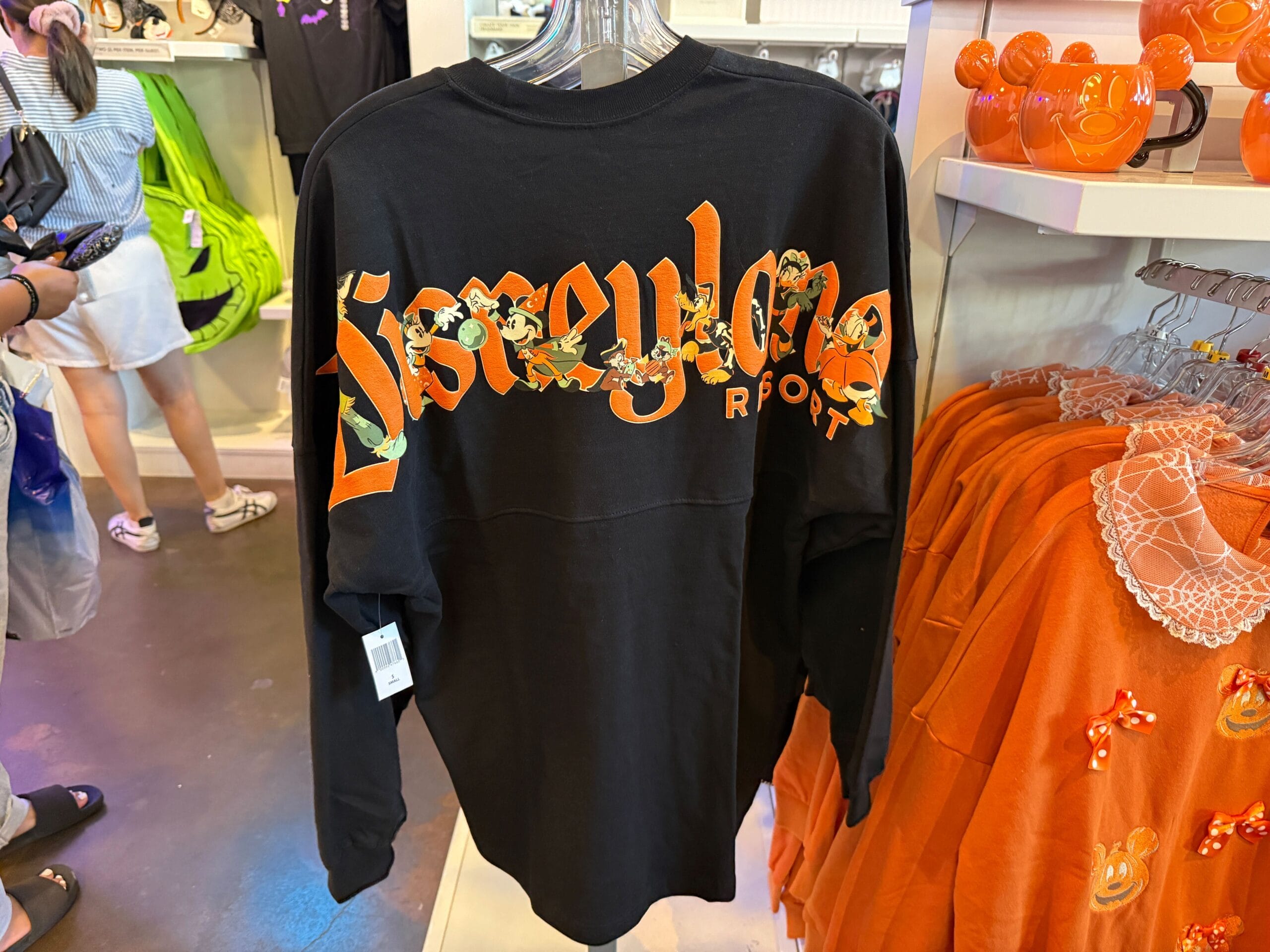 Black Disneyland Resort sweatshirt with orange floral lettering, part of the Pumpkin Merch display surrounded by orange items.