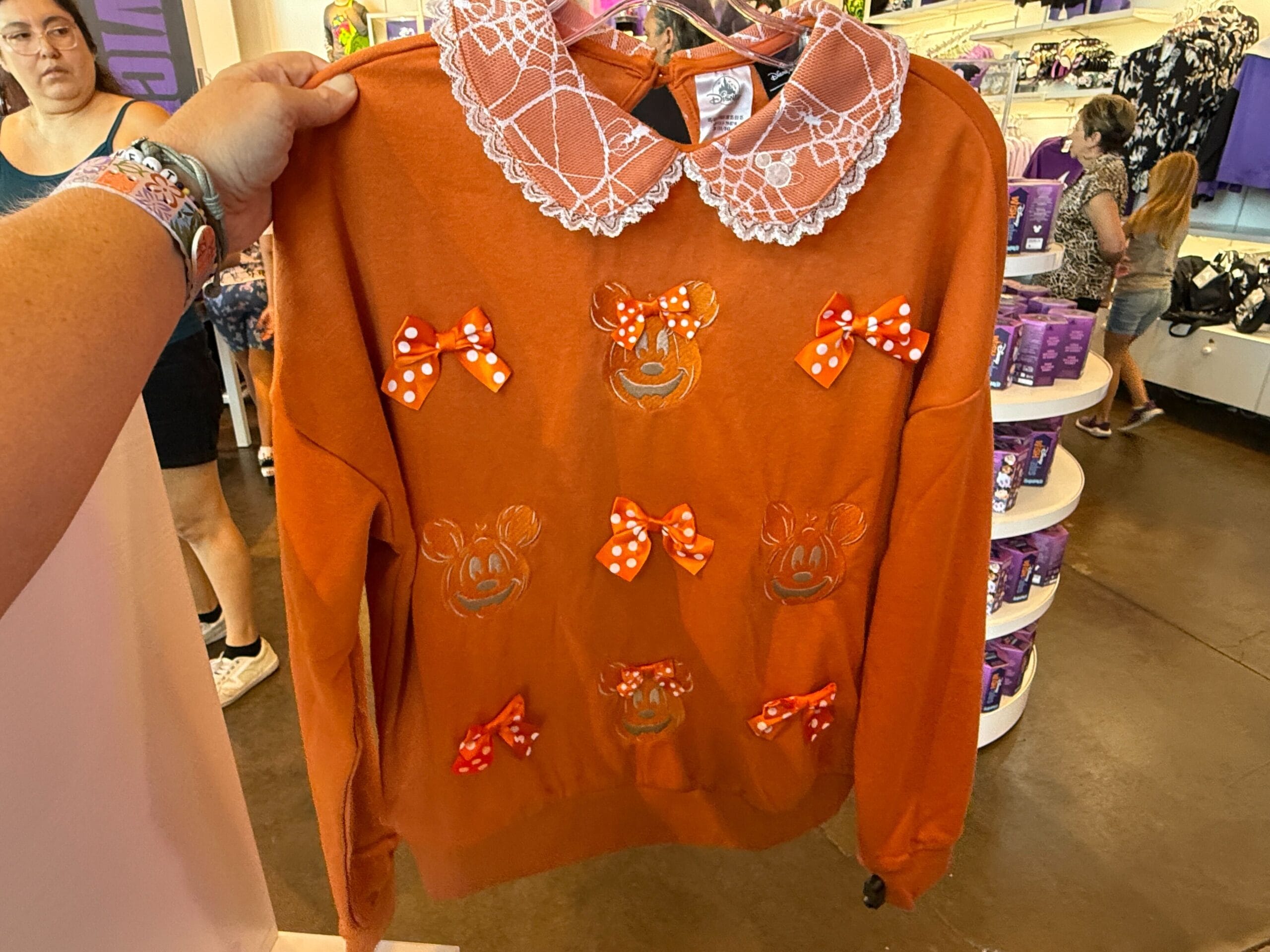 Orange sweatshirt with lace collar, Minnie Mouse faces—perfect Pumpkin Clothing for fans, displayed in-store.