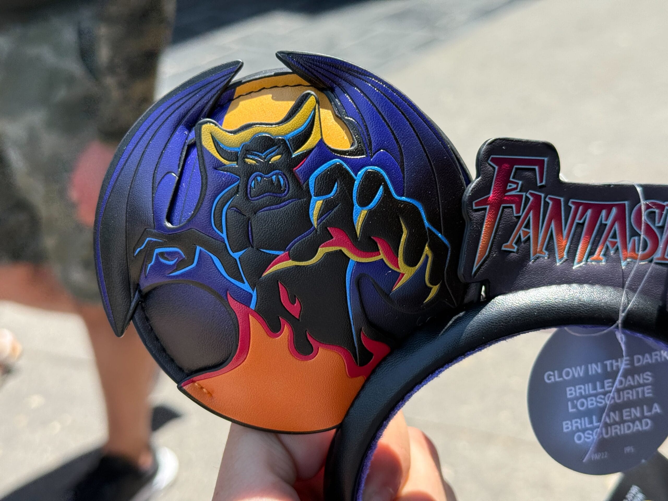 A person holds a Fantasmic Ear Headband from Disneyland Resort, featuring Chernabog and colorful fantasy flames.