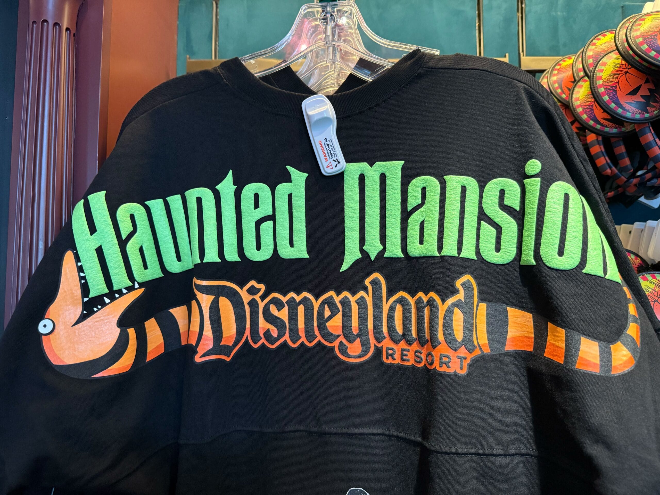 Haunted Mansion Holiday shirt with bold green and orange text and an orange-striped snake graphic.