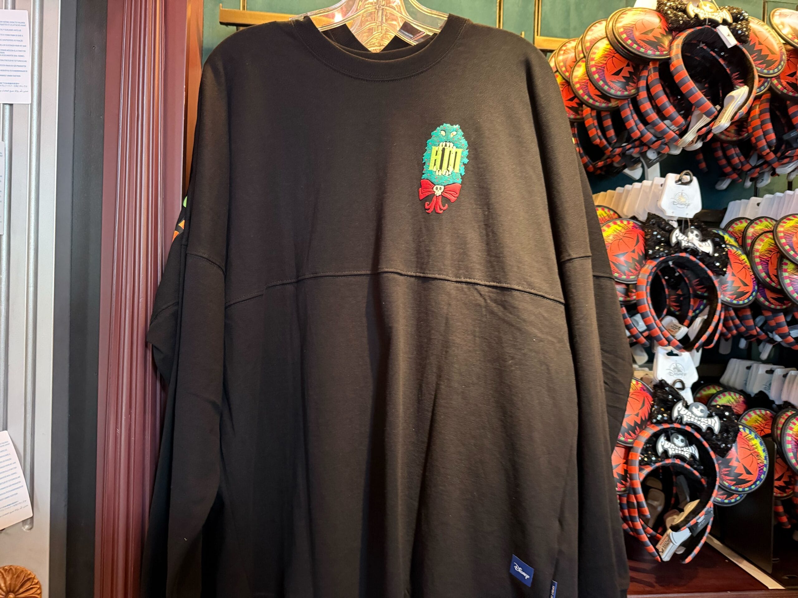 Black long-sleeve shirt with a colorful embroidered wreath, perfect for Haunted Mansion Holiday merch displays in-store.