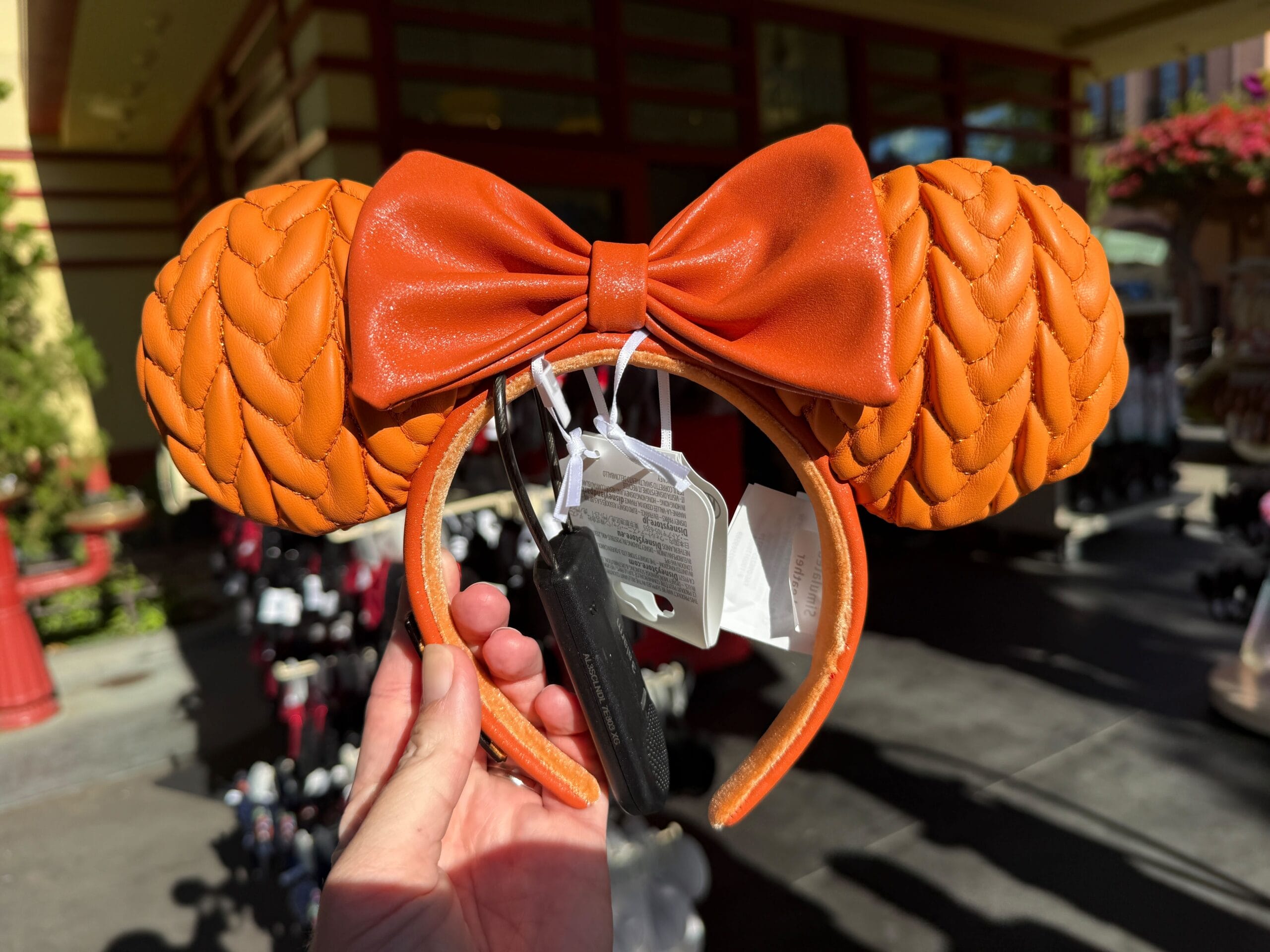 Hand holding an orange pumpkin-themed Minnie Mouse ear headband with a large bow at Disneyland Resort during Halloween season.