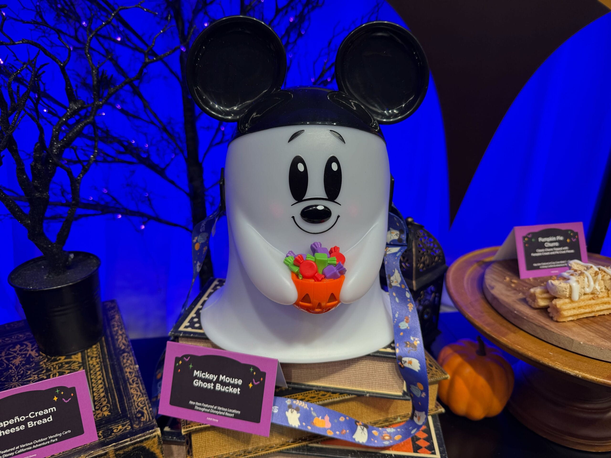 A Mickey Mouse ghost bucket holding candy, displayed on a table with Halloween decorations and treats.