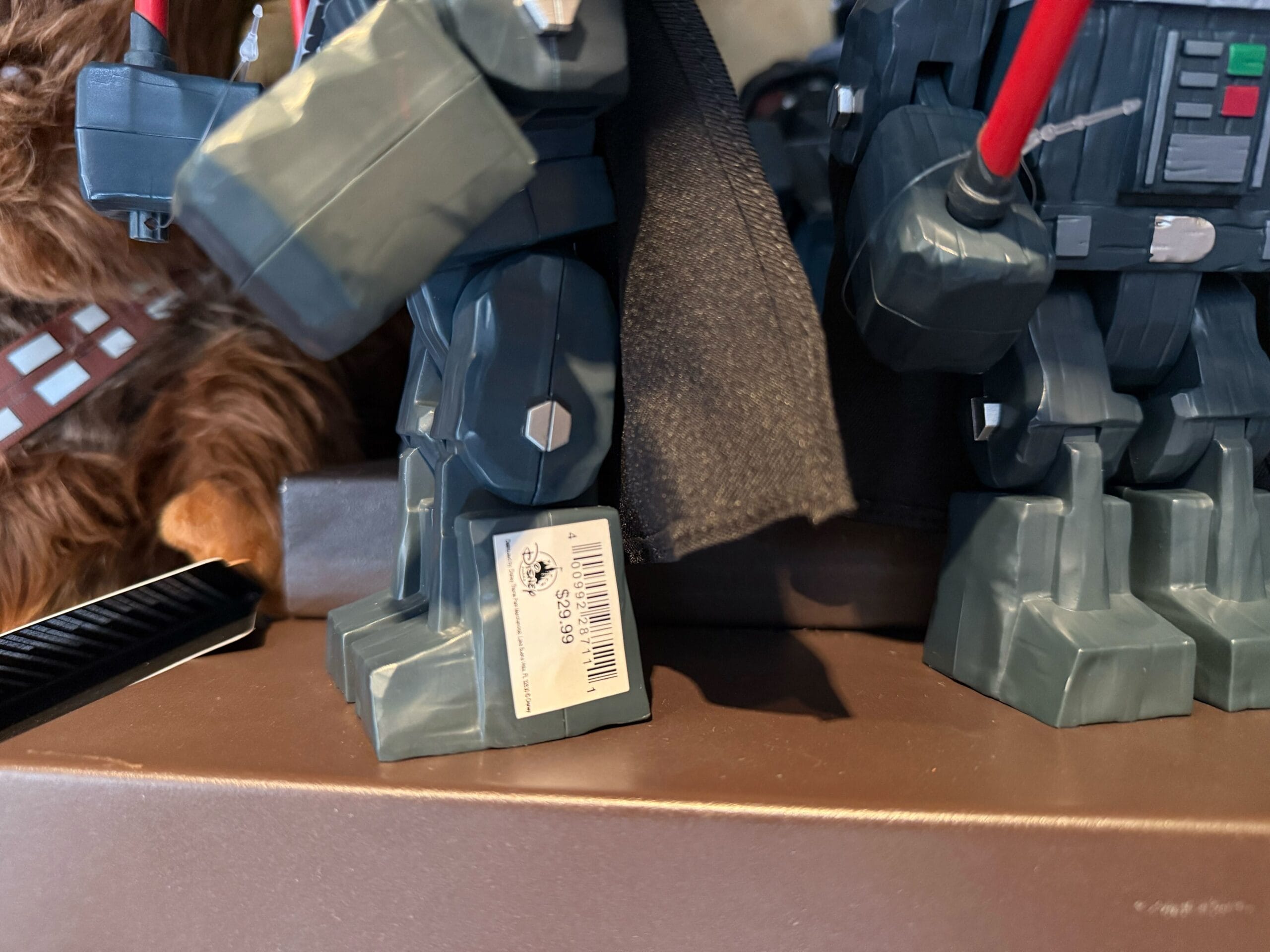 A close-up of toy robot legs, one with a price tag and barcode, stands beside a Chewbacca figure and R2-D2.
